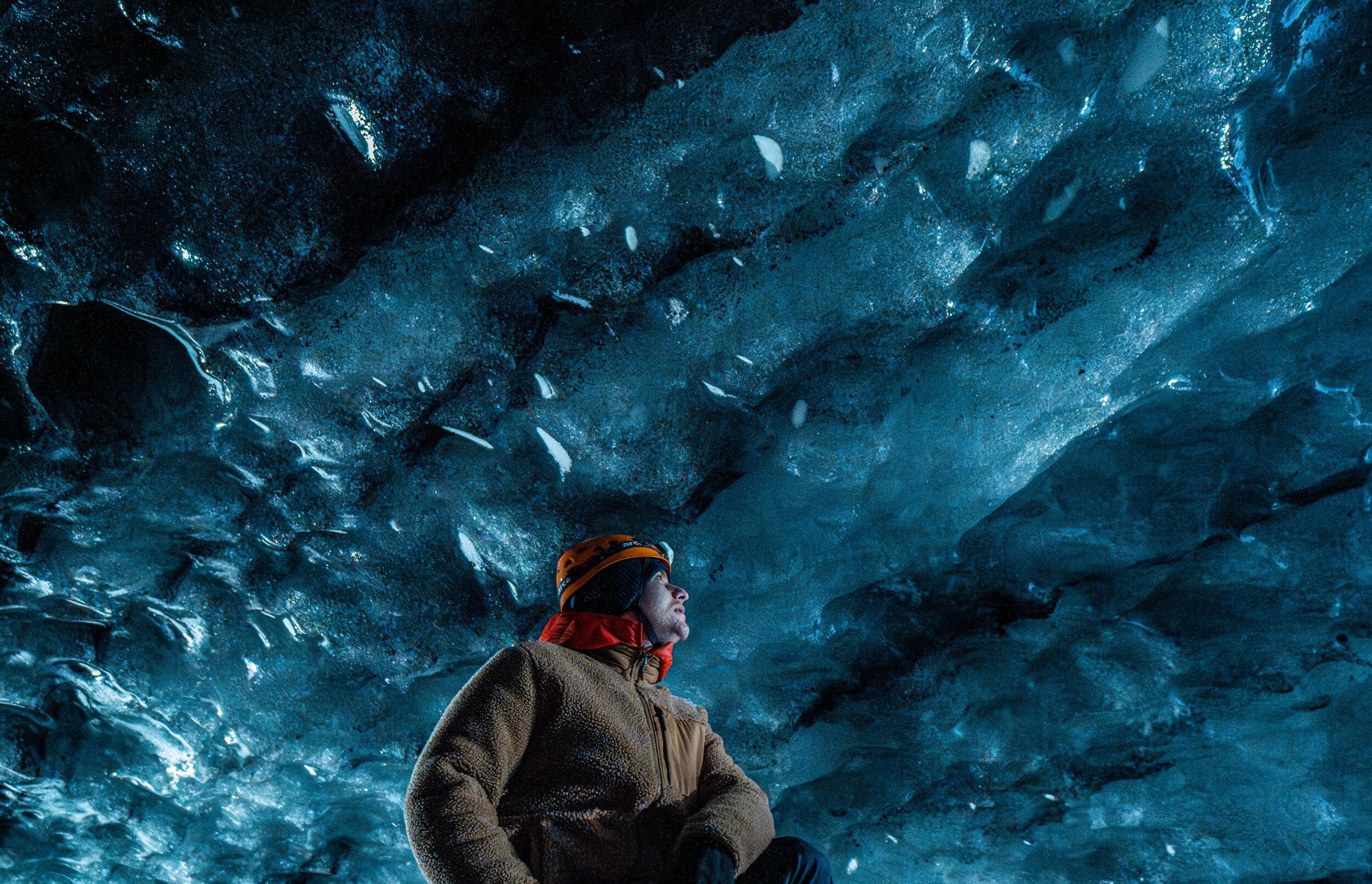 a man is sitting in an ice cave looking up at the sky .