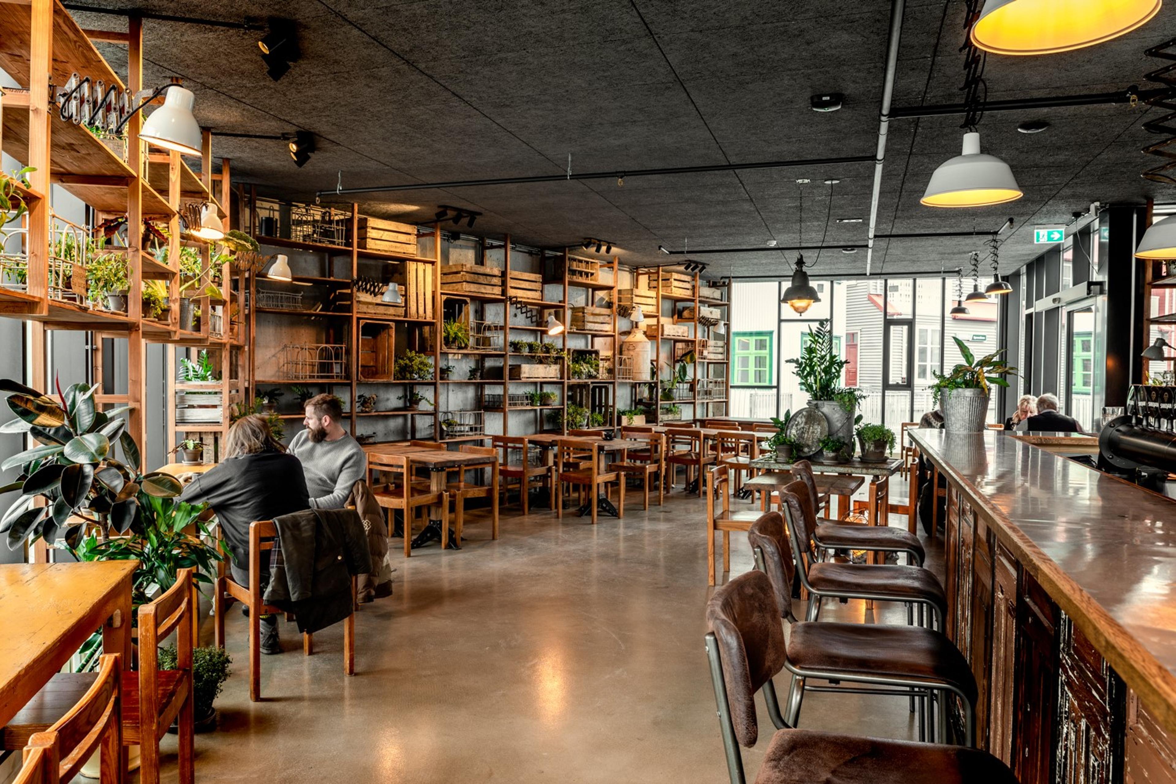 Spacious interior of The Old Dairy Food Hall in Selfoss, featuring wooden tables, shelves with plants, and people dining in a cozy, rustic ambiance.