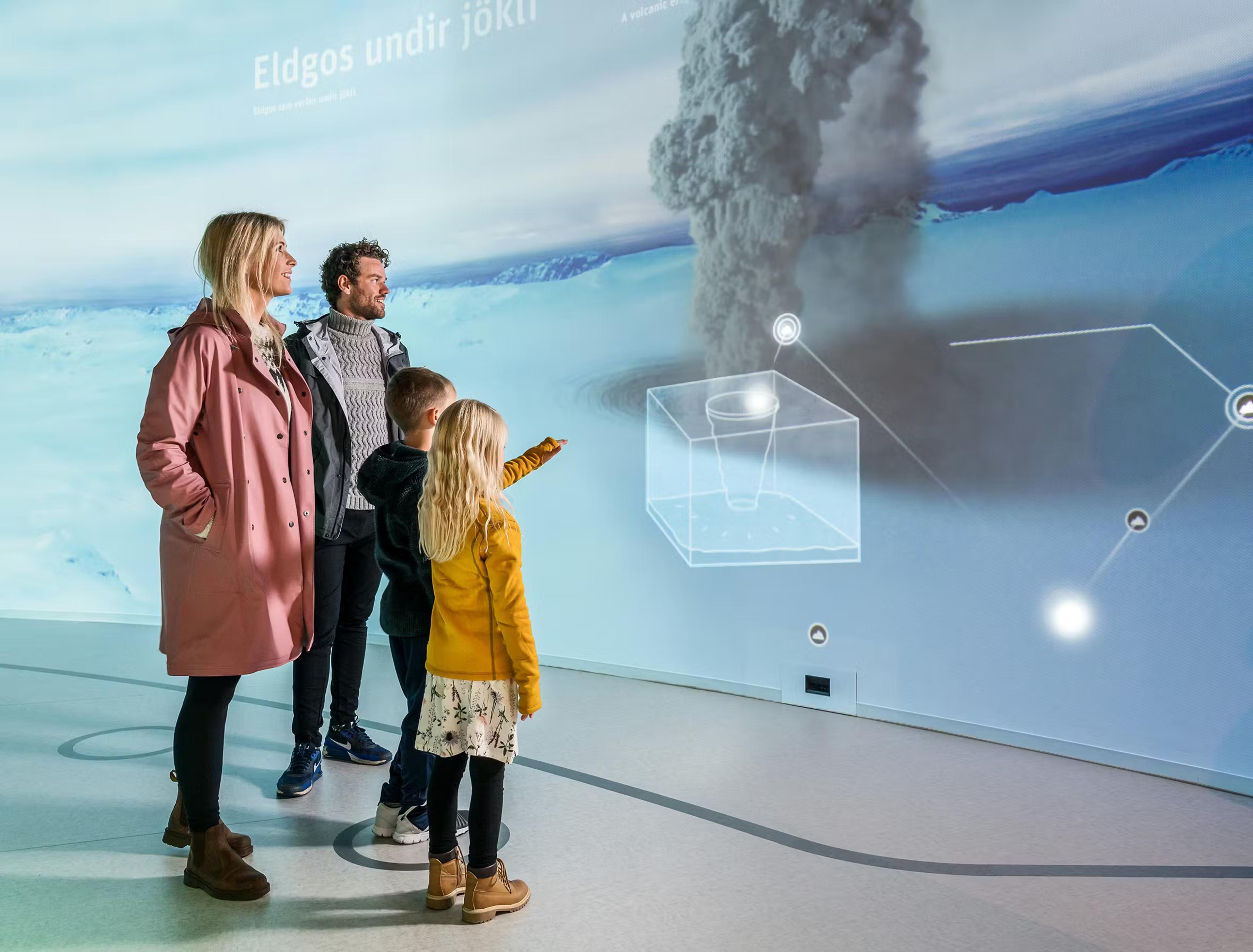 Family views a museum exhibit showing a subglacial volcanic eruption and scientific diagrams projected on a large wall.