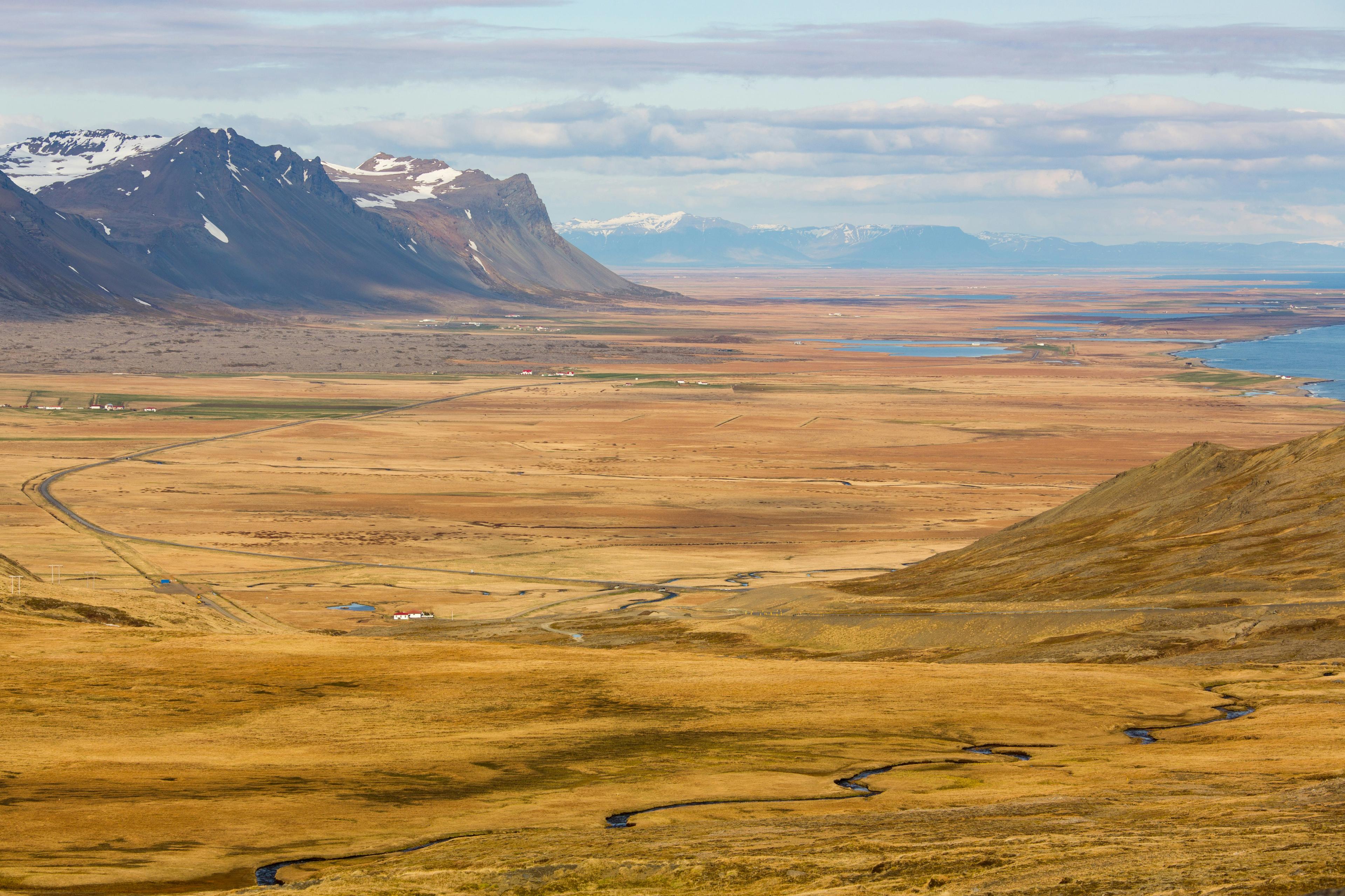 A breathtaking panoramic view of the Snæfellsnes Peninsula in Iceland, showcasing vast golden fields, winding roads, and rugged snow-capped mountains under a clear blue sky.