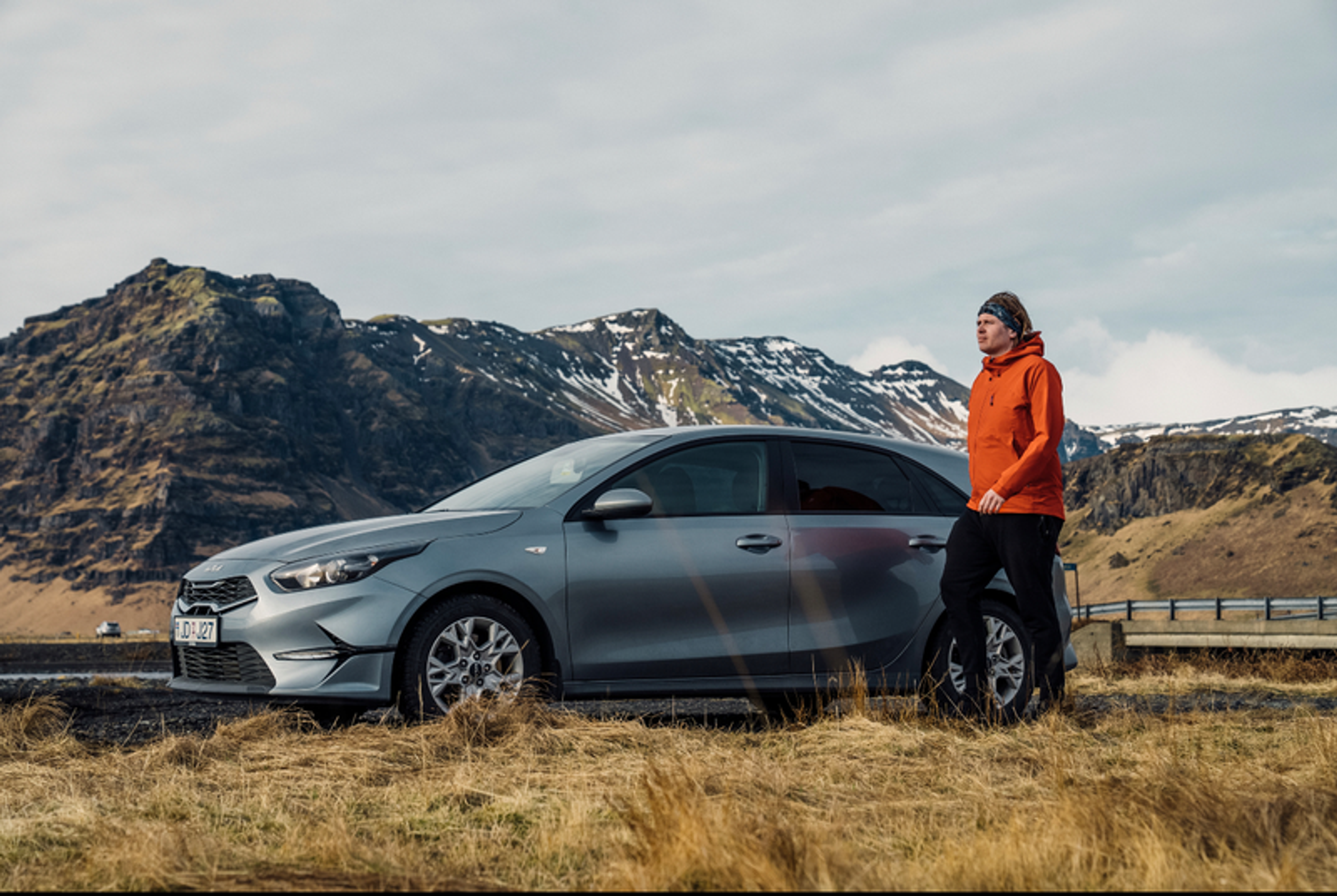  A person stands beside a parked car against a scenic mountain backdrop in Iceland, highlighting an ideal car rental spot.