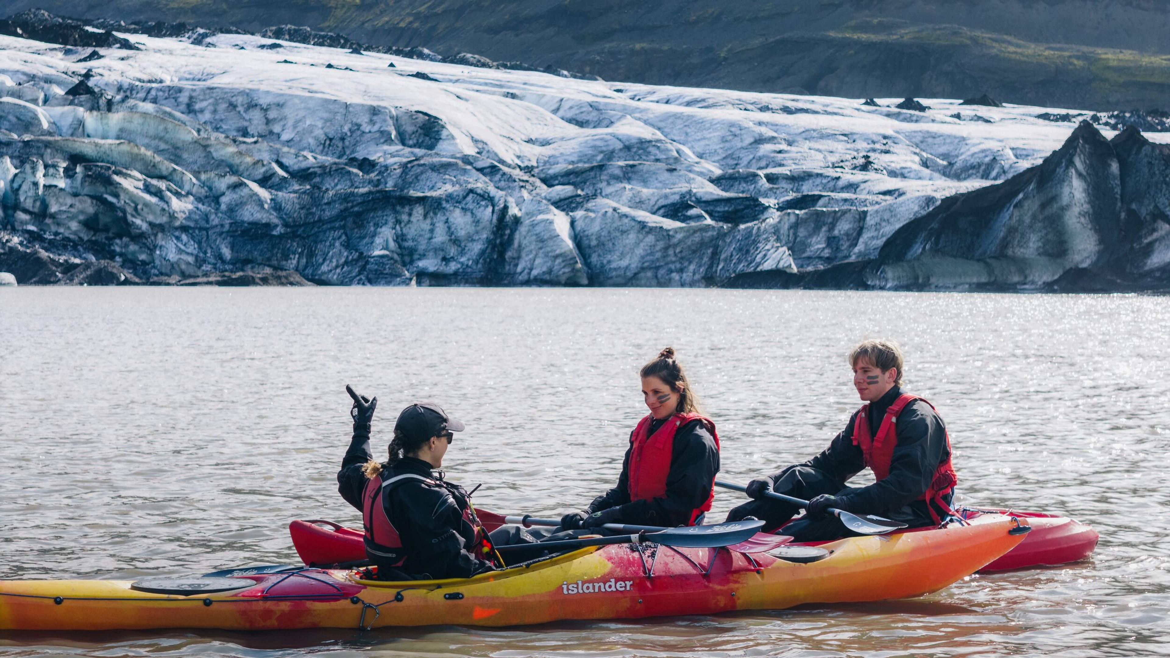 Three people kayak on a lake in front of a glacier in Iceland
