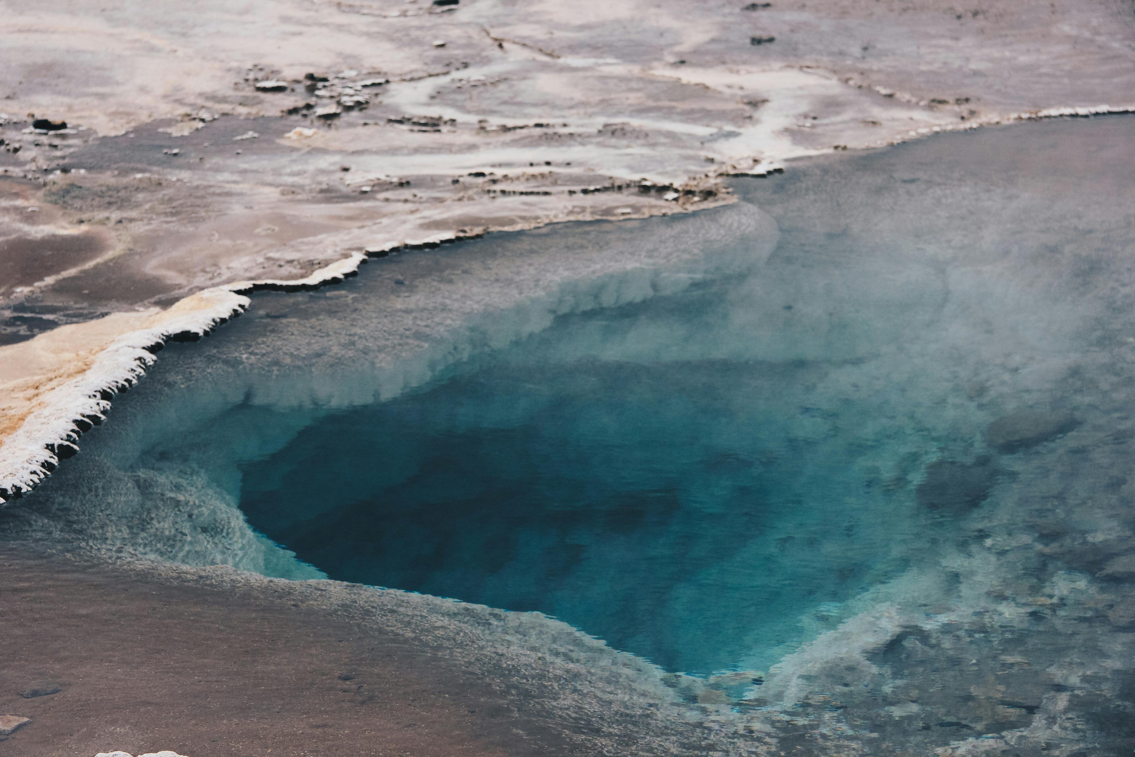 Close-up of a geothermal hot spring in Iceland, with steam rising from the vivid blue water and contrasting with the earthy tones of the surrounding mineral-rich terrain.