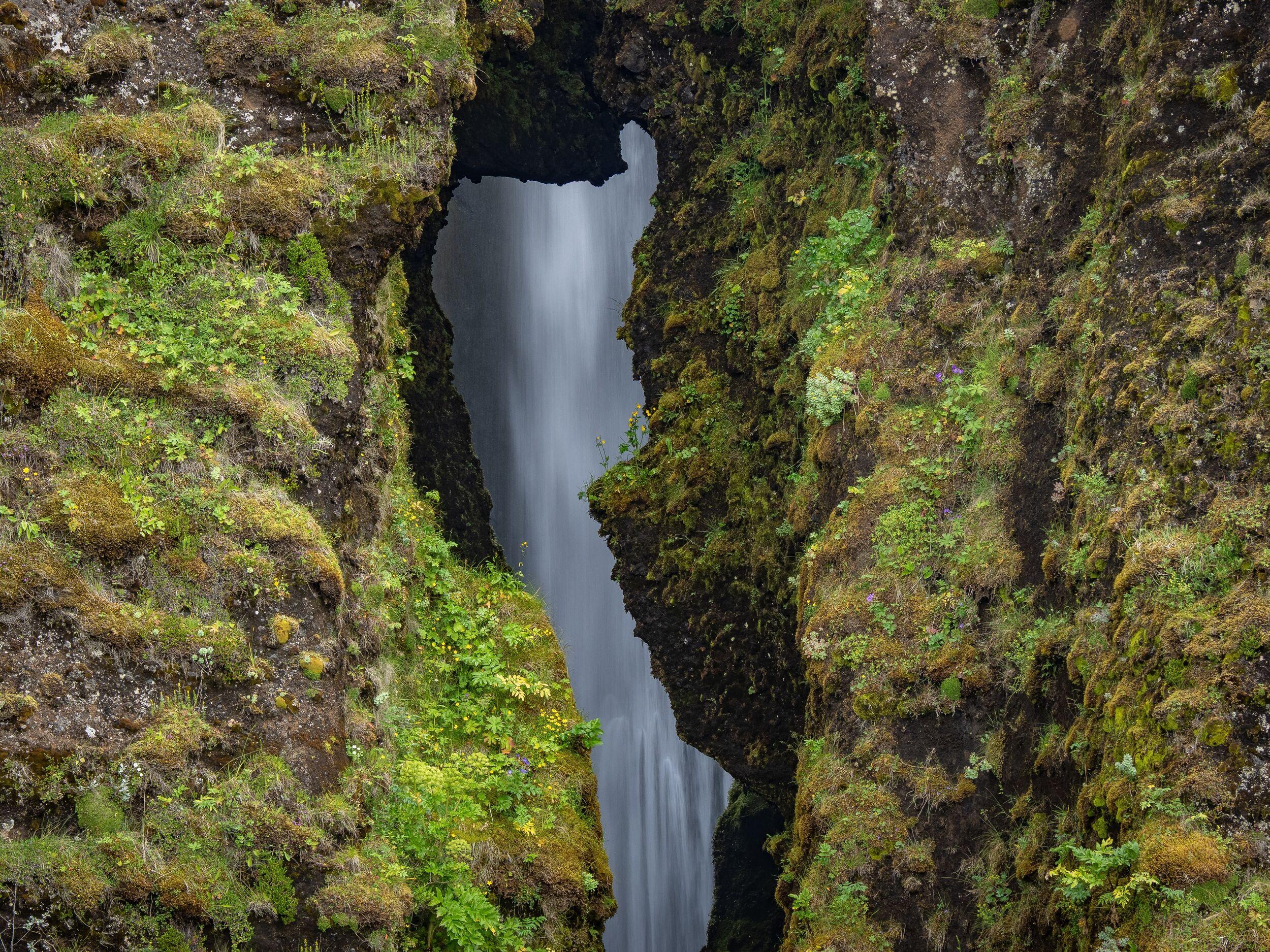 A waterfall streams through a narrow, moss-covered rock crevice.