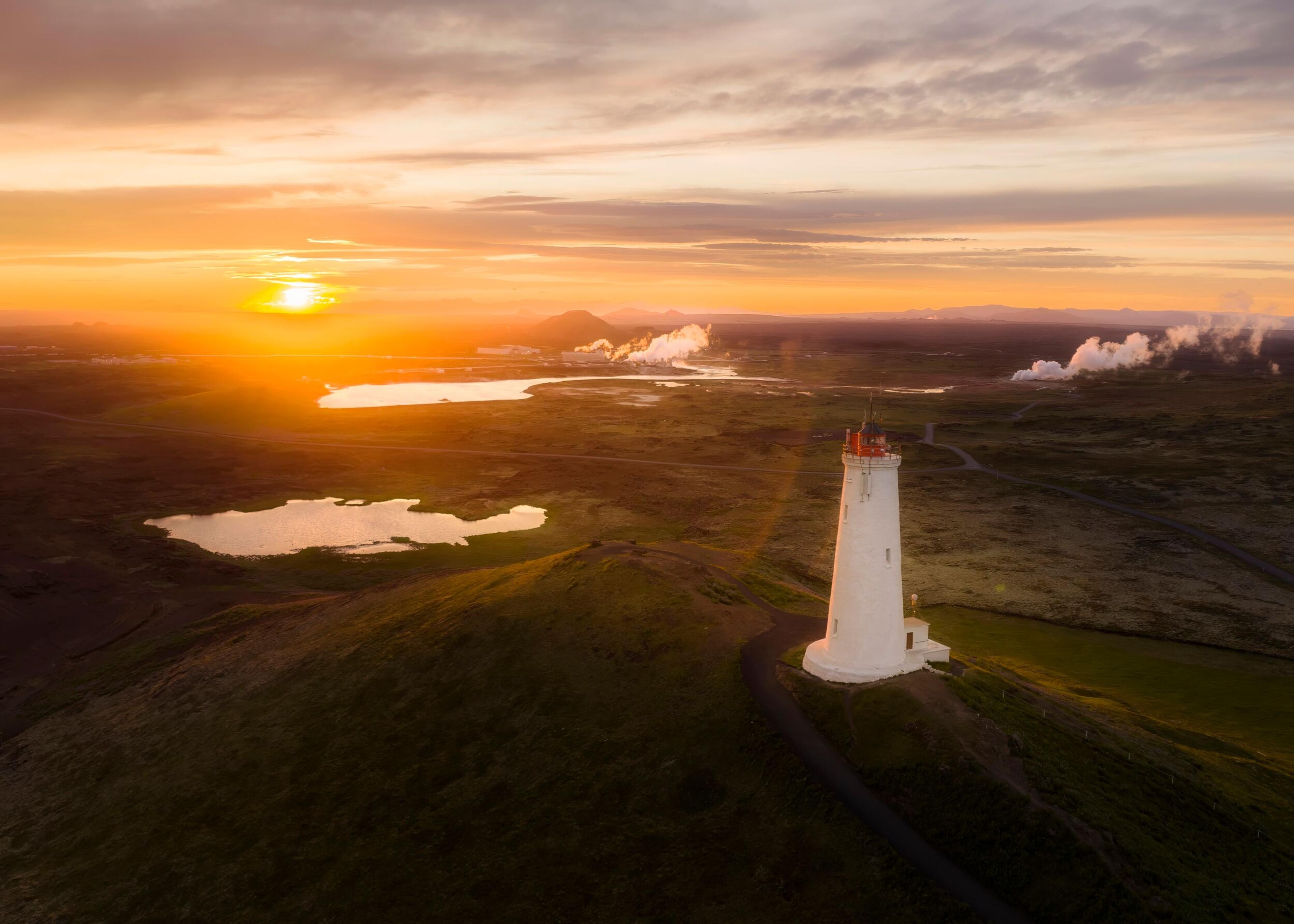 A white lighthouse sitting on a hilltop with the sunset painting the landscape gold