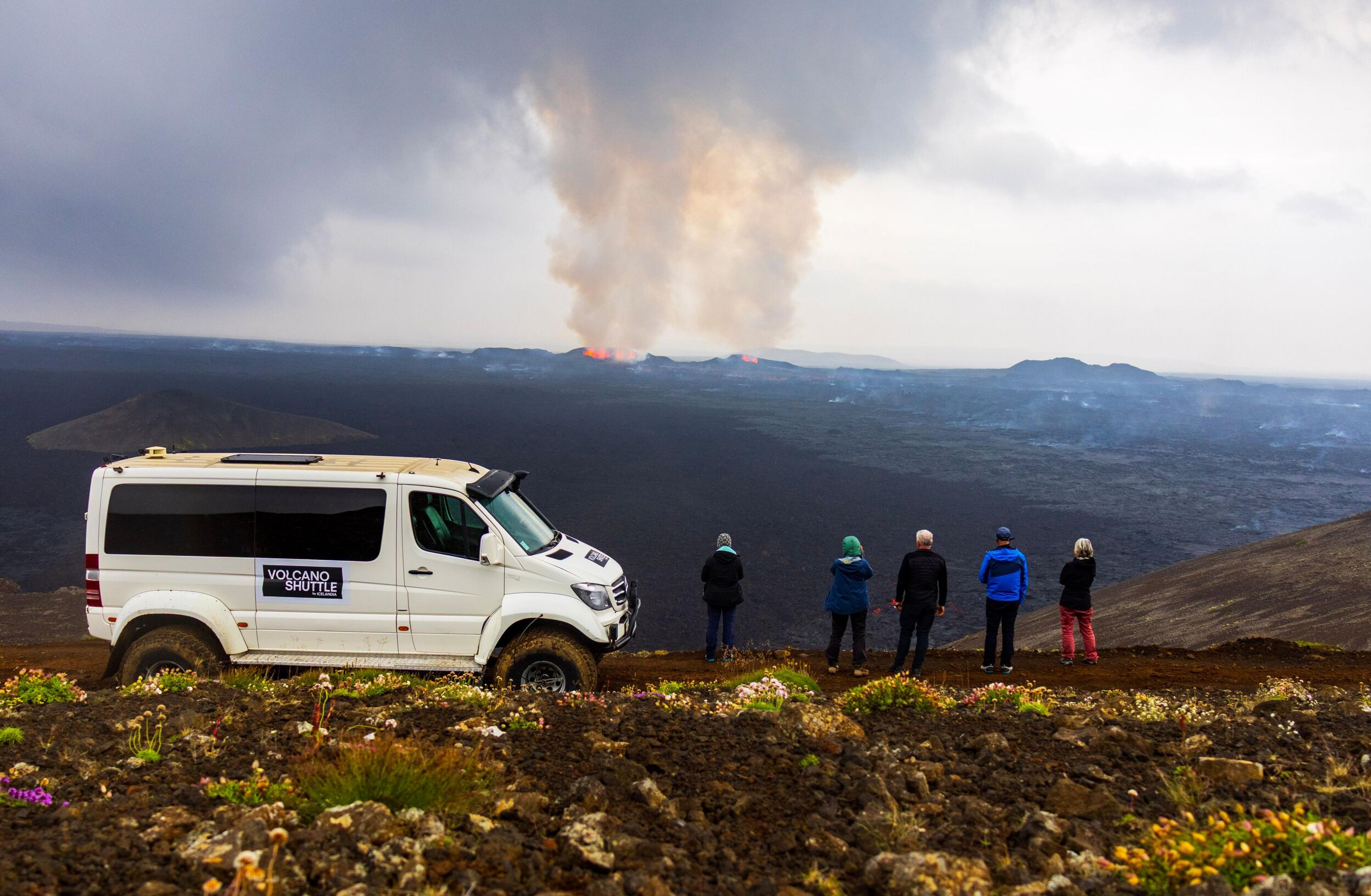 a group of people are standing on top of a mountain looking at a volcano .