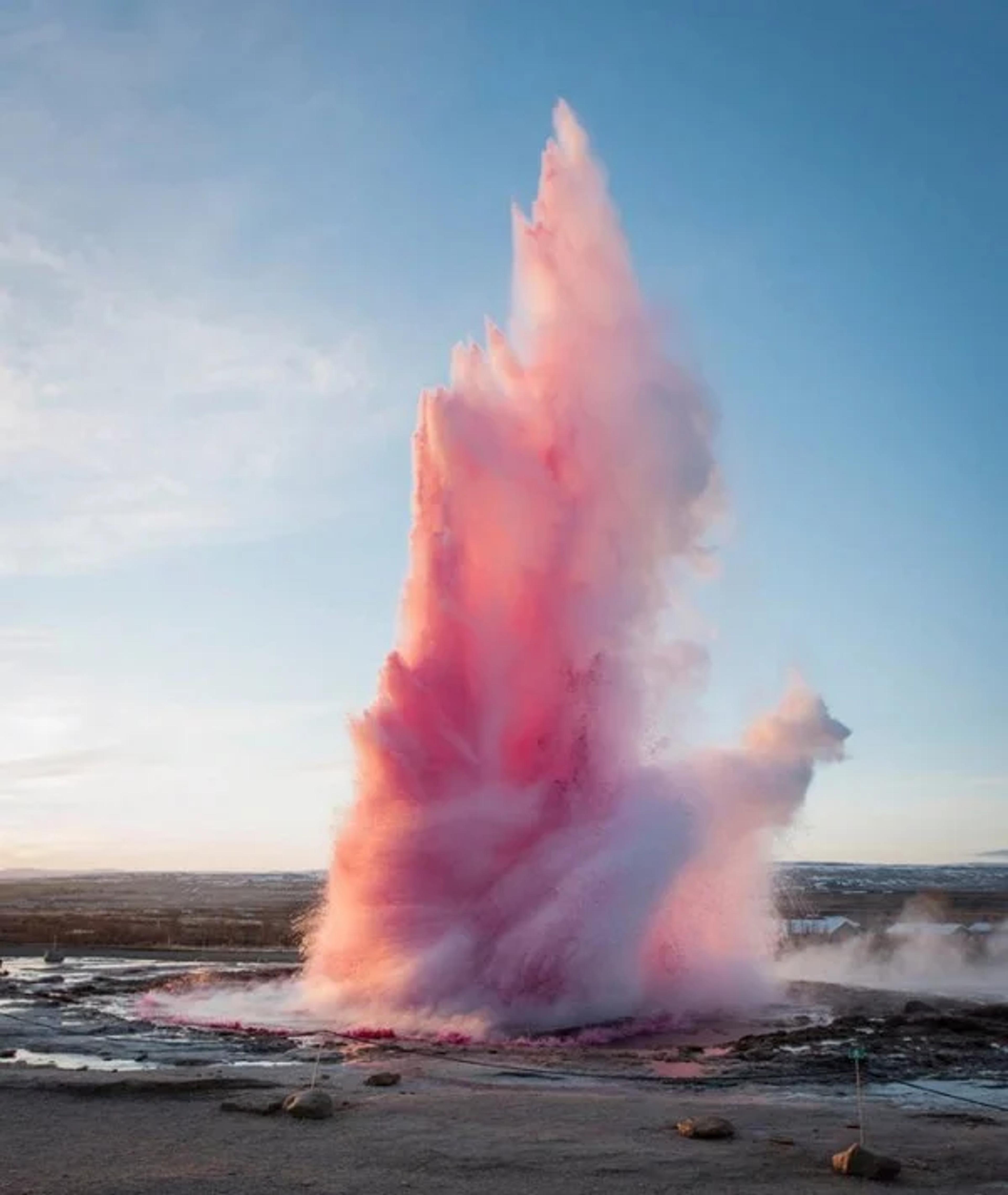 A geyser eruption with water painted in pink hues at the Geysir geothermal area in Iceland.