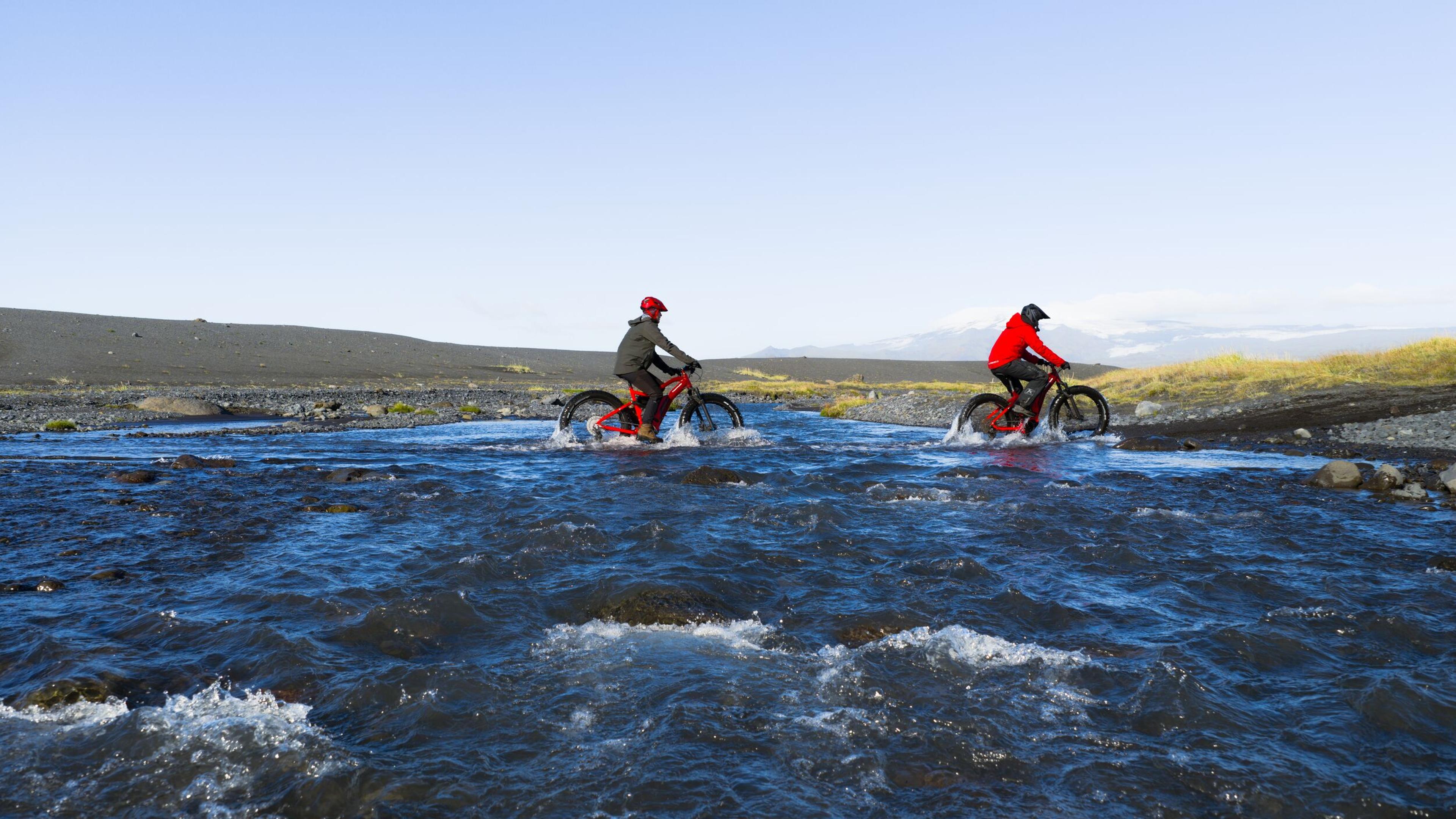 two people are riding bikes through a river .