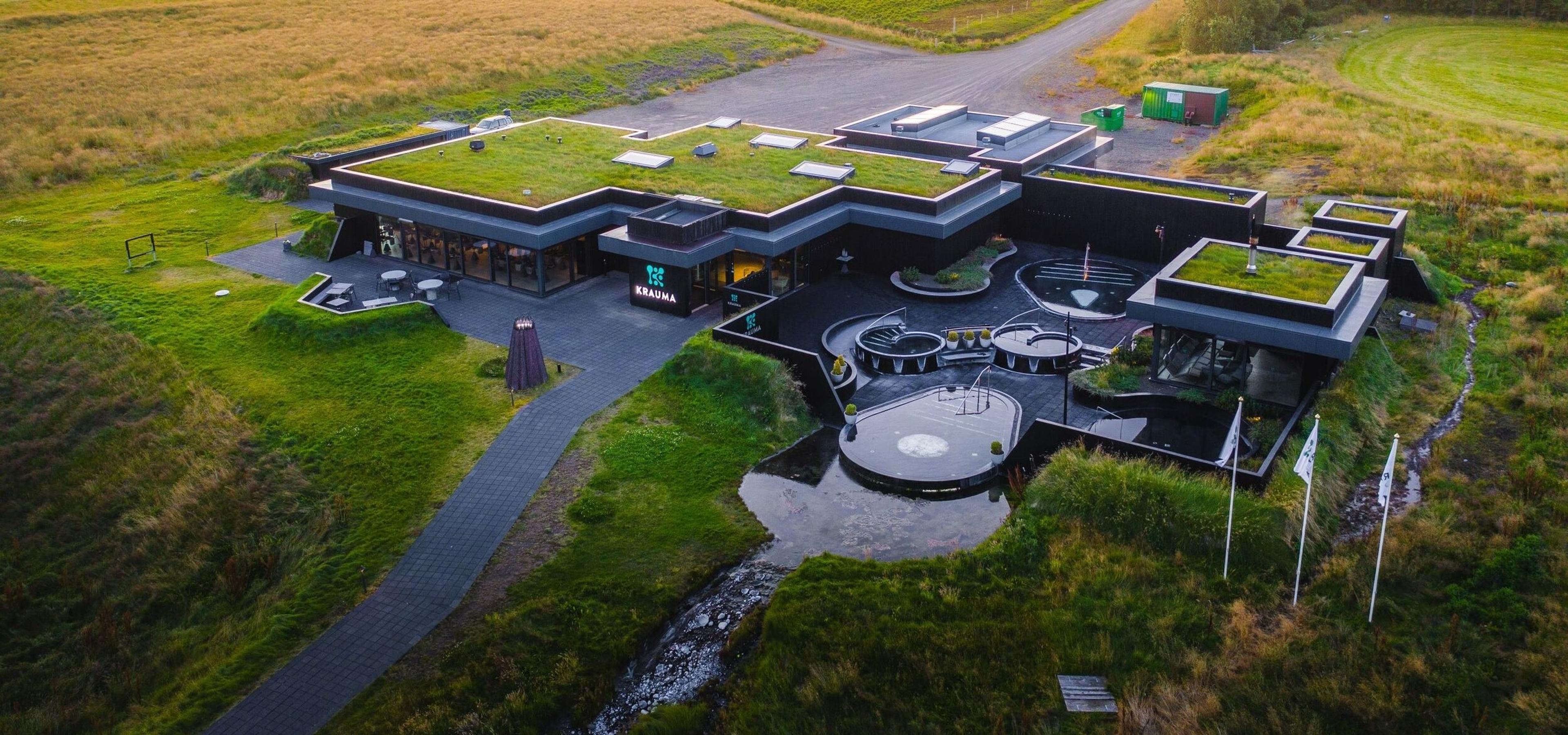 Aerial view of Krauma geothermal baths, featuring modern black stone pools filled with natural hot water sourced from Deildartunguhver, surrounded by sleek architecture and lush Icelandic countryside.