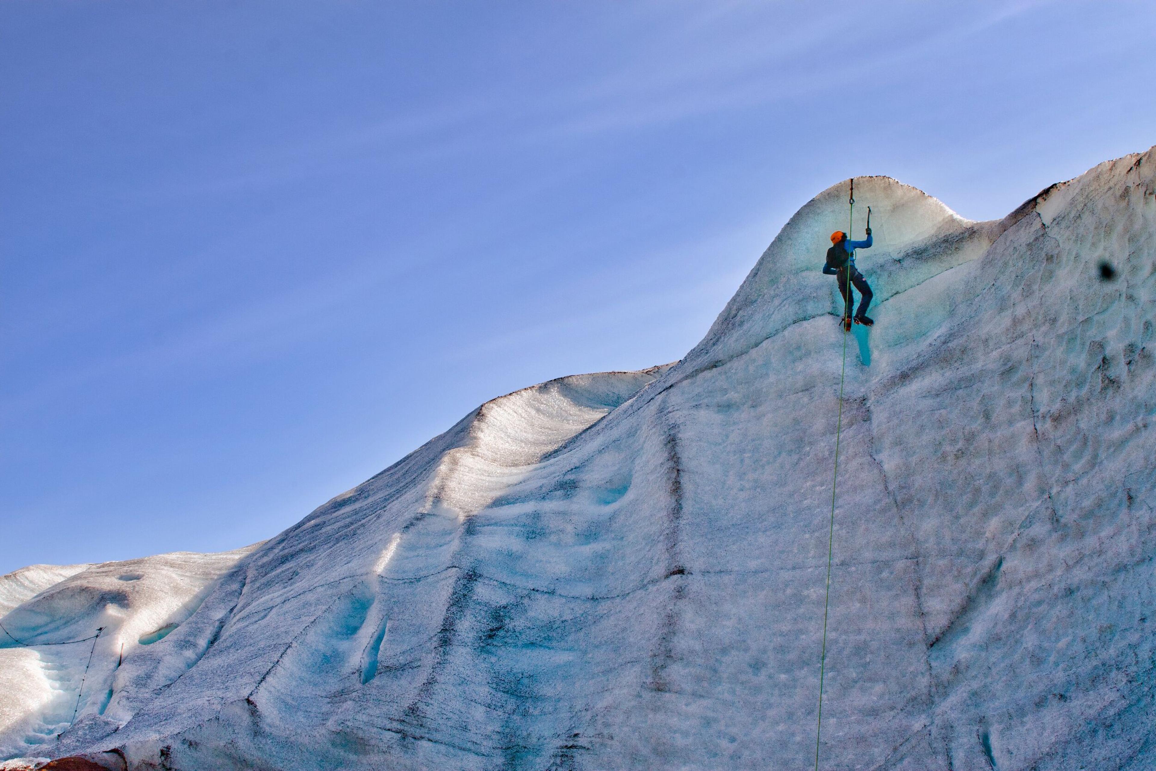 A person climbing up an ice wall using a rope and ice axes