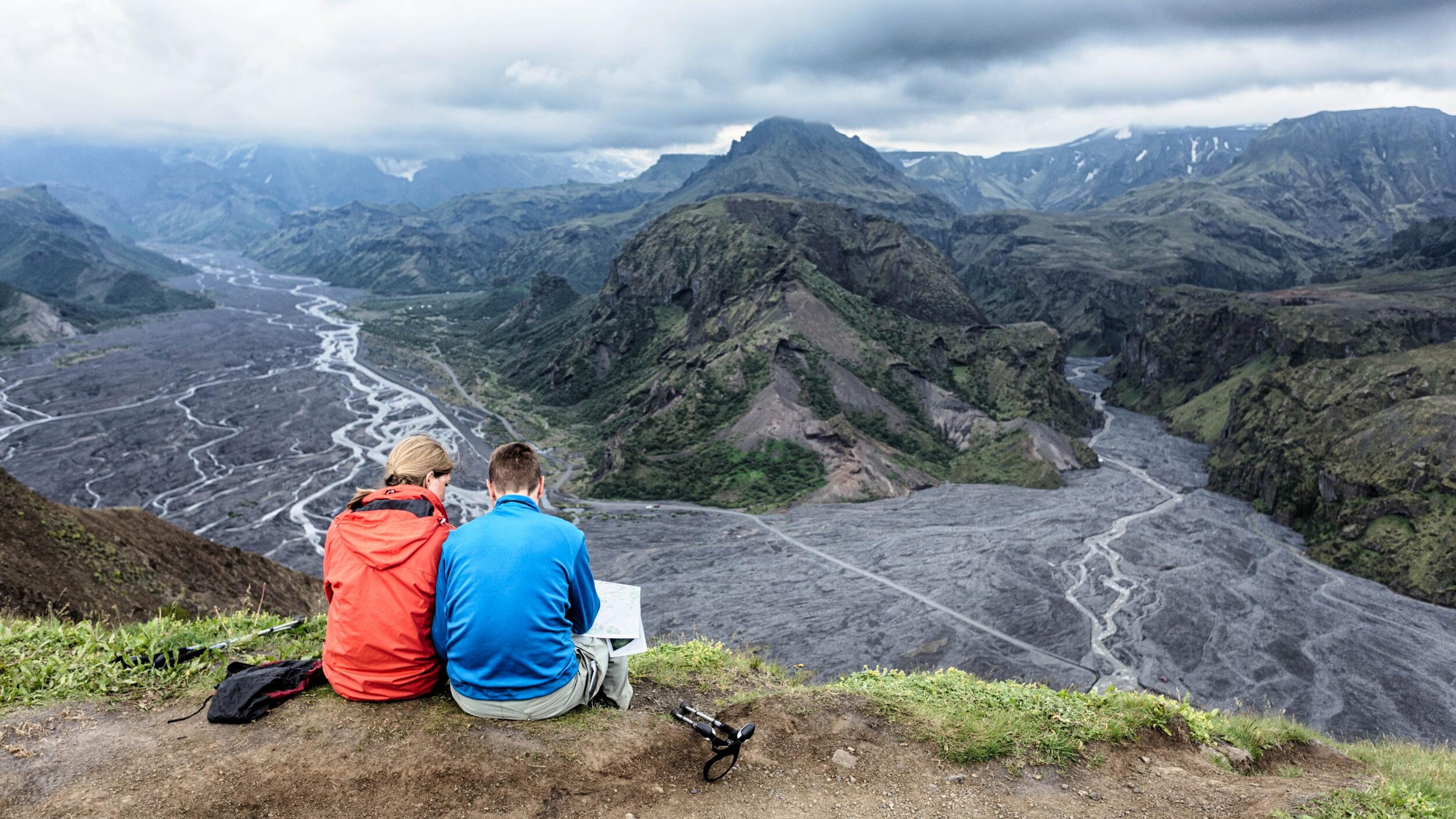 A couple sitting by a cliff admiring the view of Þórsmörk Valley in the Icelandic Highlands.