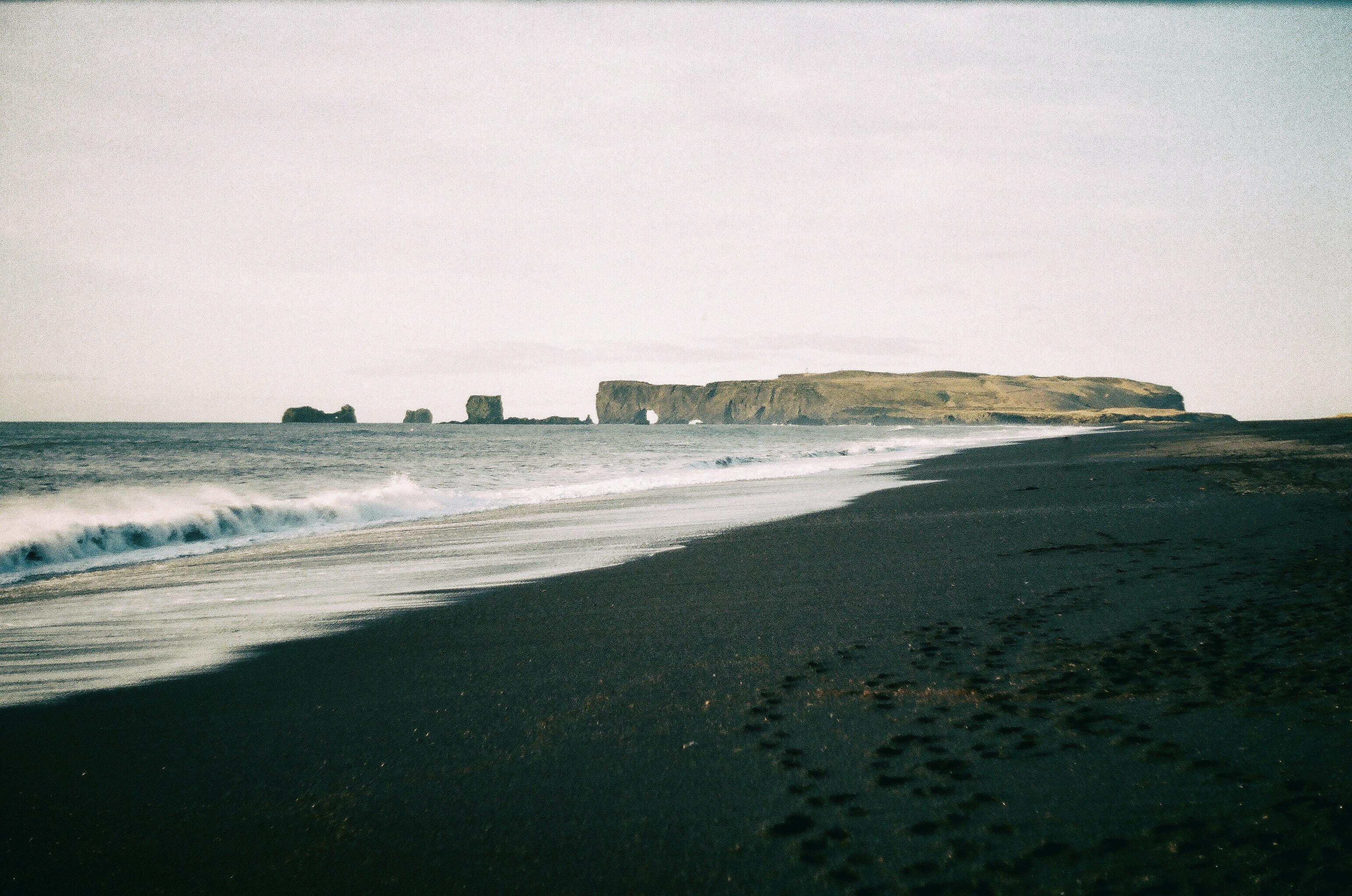 Dyrhólaey arch and its surrounding cliffs sit beside a peaceful black sand beach, a scenic stop on Iceland South Coast tours.