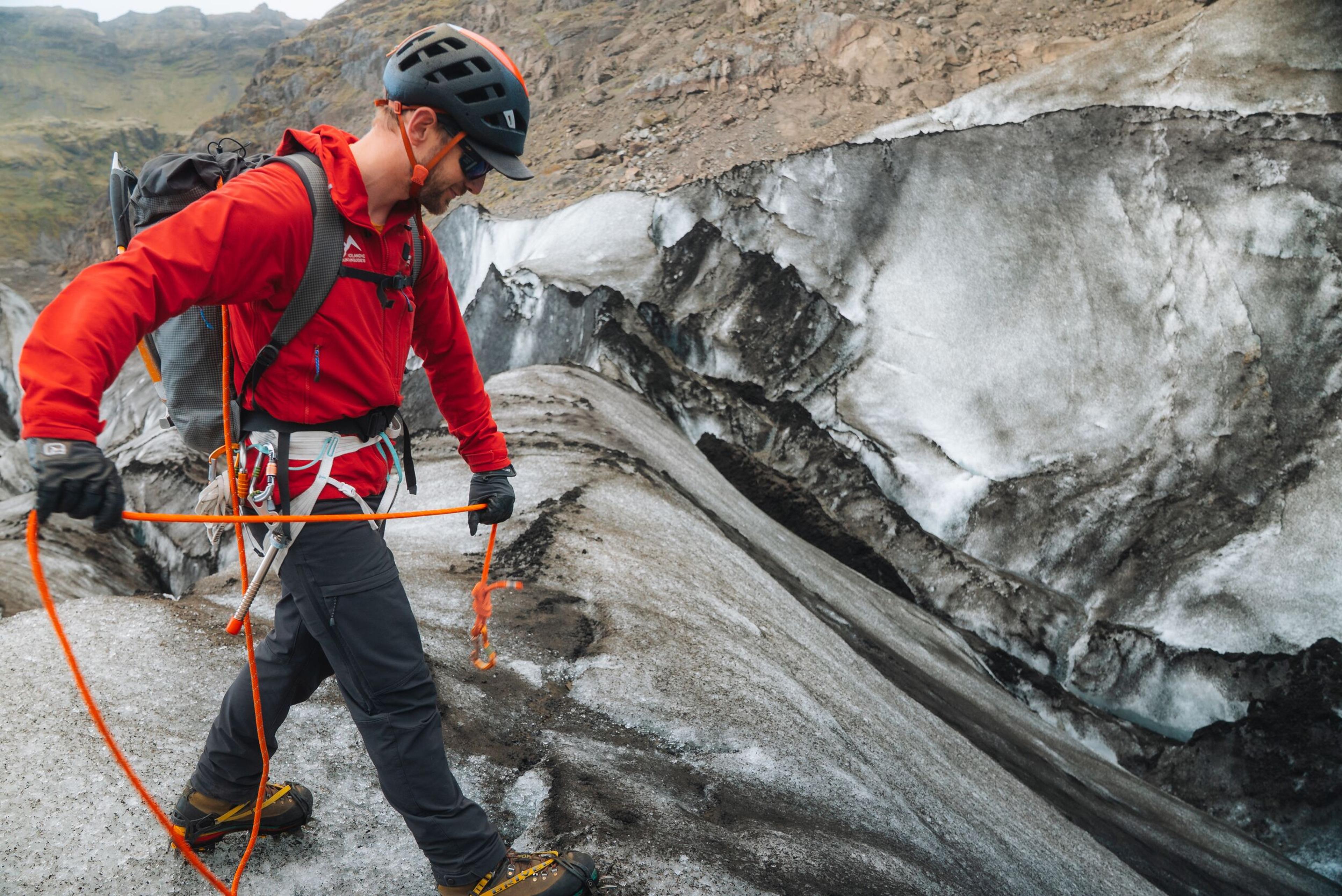 a man in a red jacket and helmet is walking on a glacier .