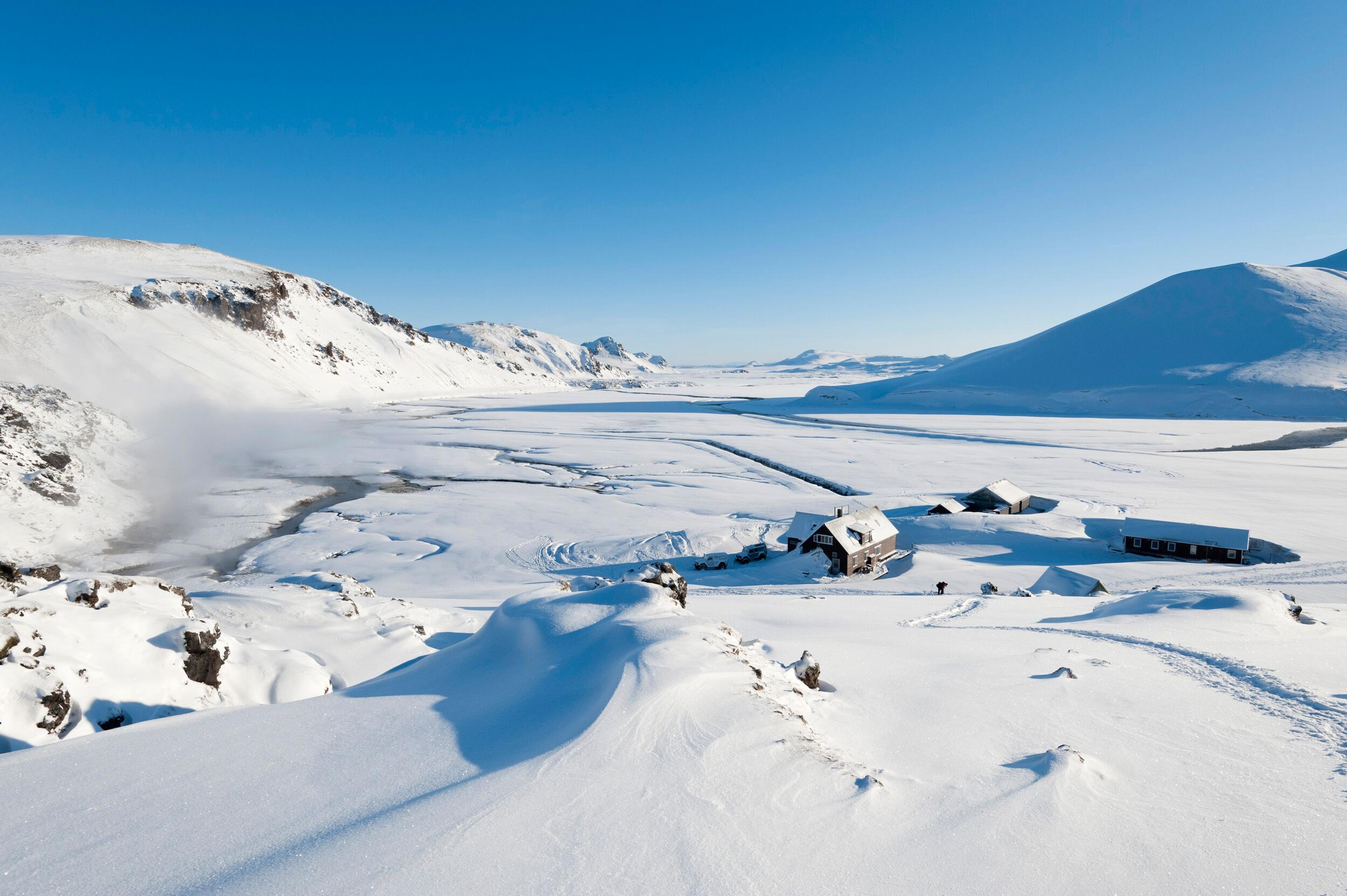 A snow-covered valley with buildings surrounded by mountains under a clear blue sky.