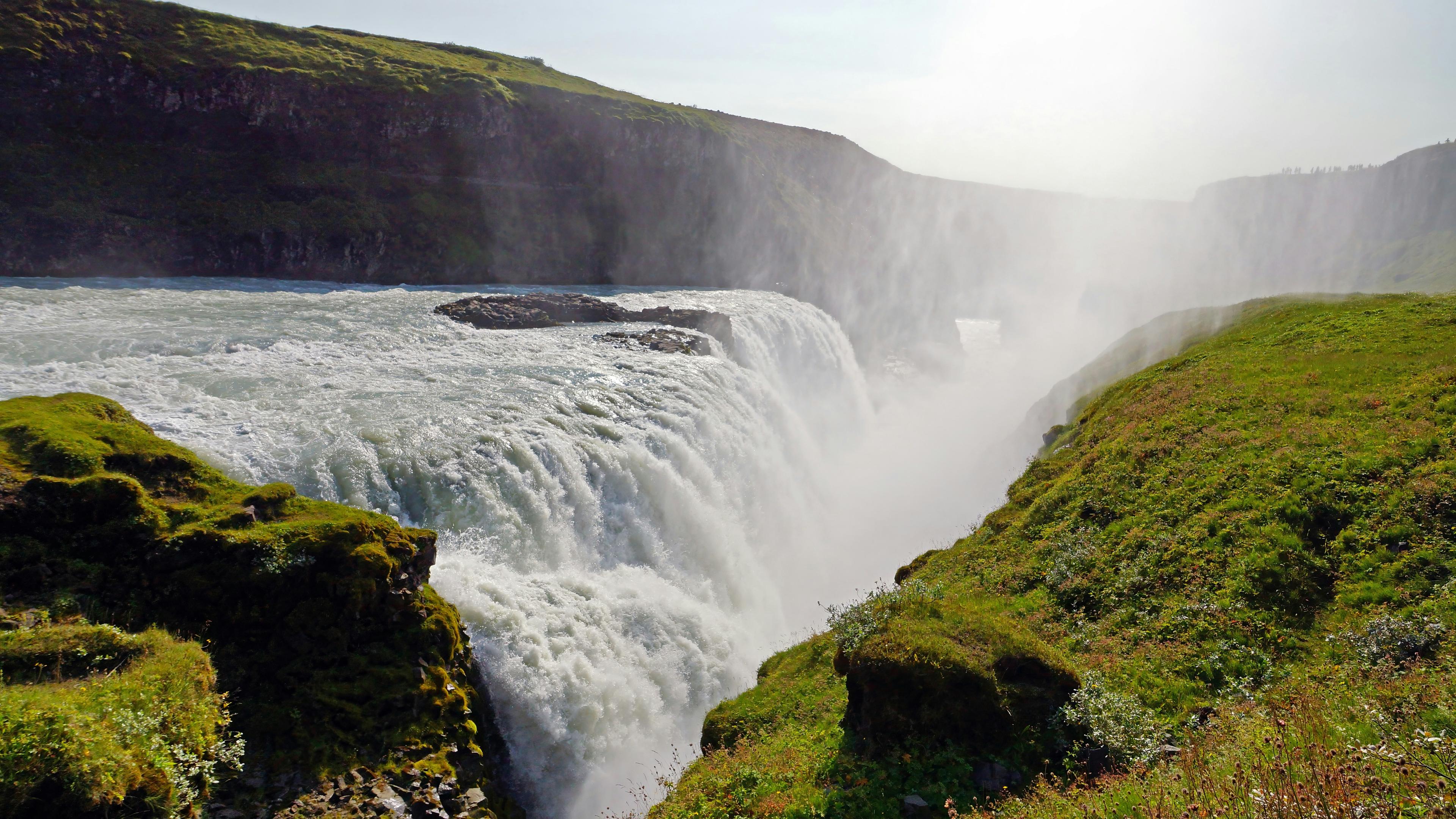 The powerful Gullfoss waterfall cascading over rugged cliffs, with mist rising into the air, framed by green mossy slopes. A must-see highlight on a private Golden Circle tour.