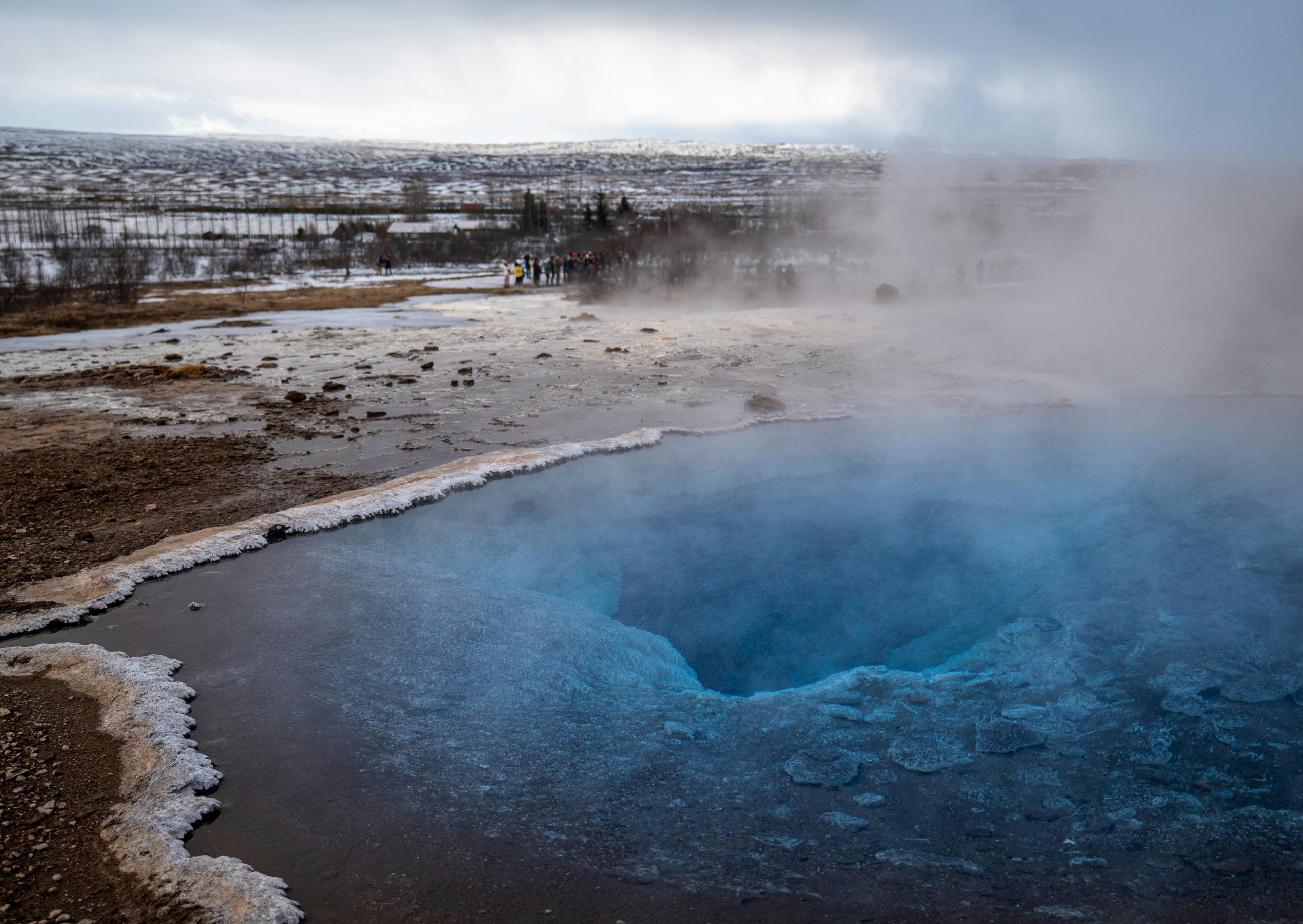 Geysir hot spring with deep blue water and steam rising, set in a snowy landscape in Iceland's Golden Circle region.