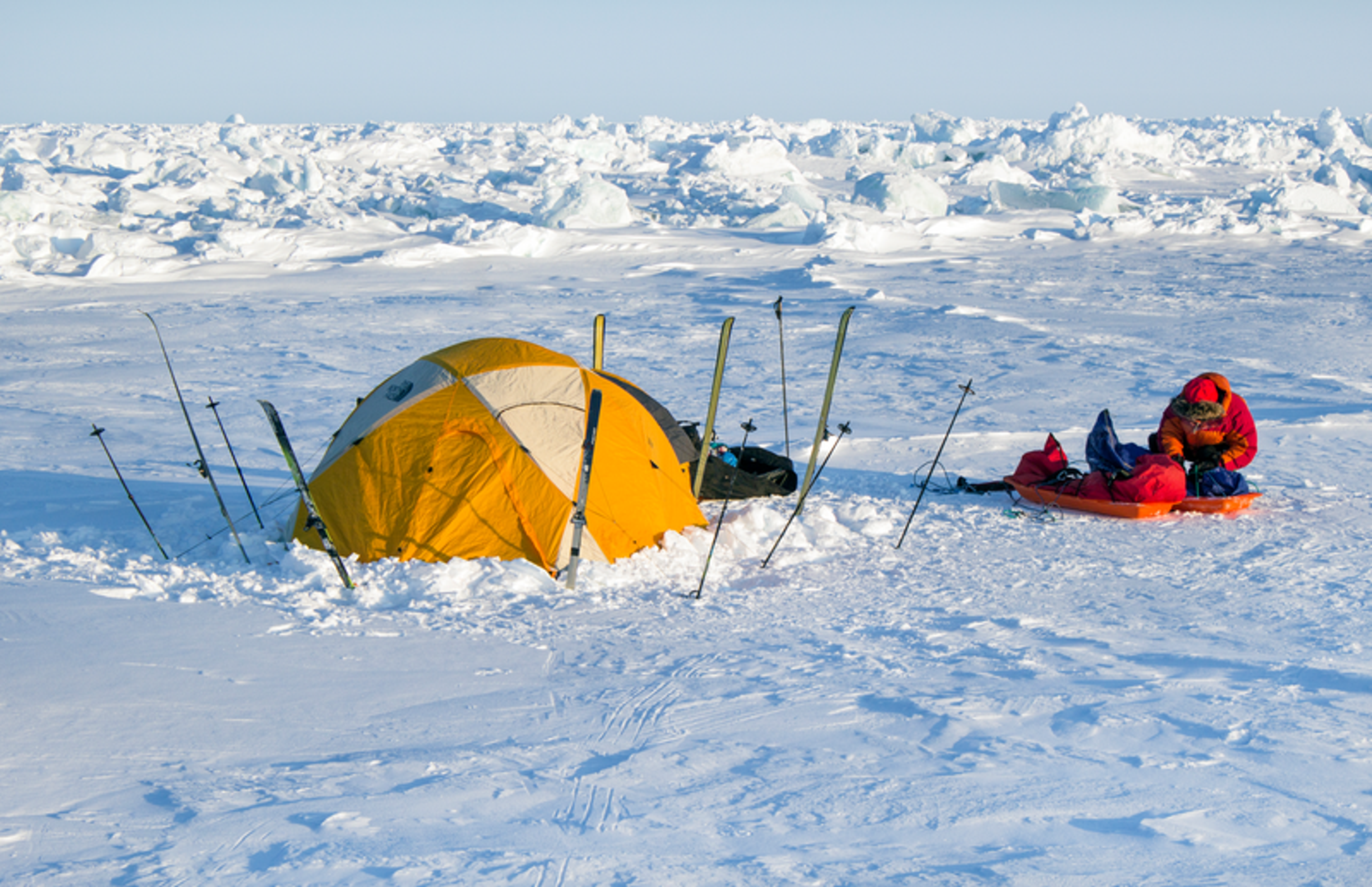A tent pitched up in the snow surrounded by walking sticks