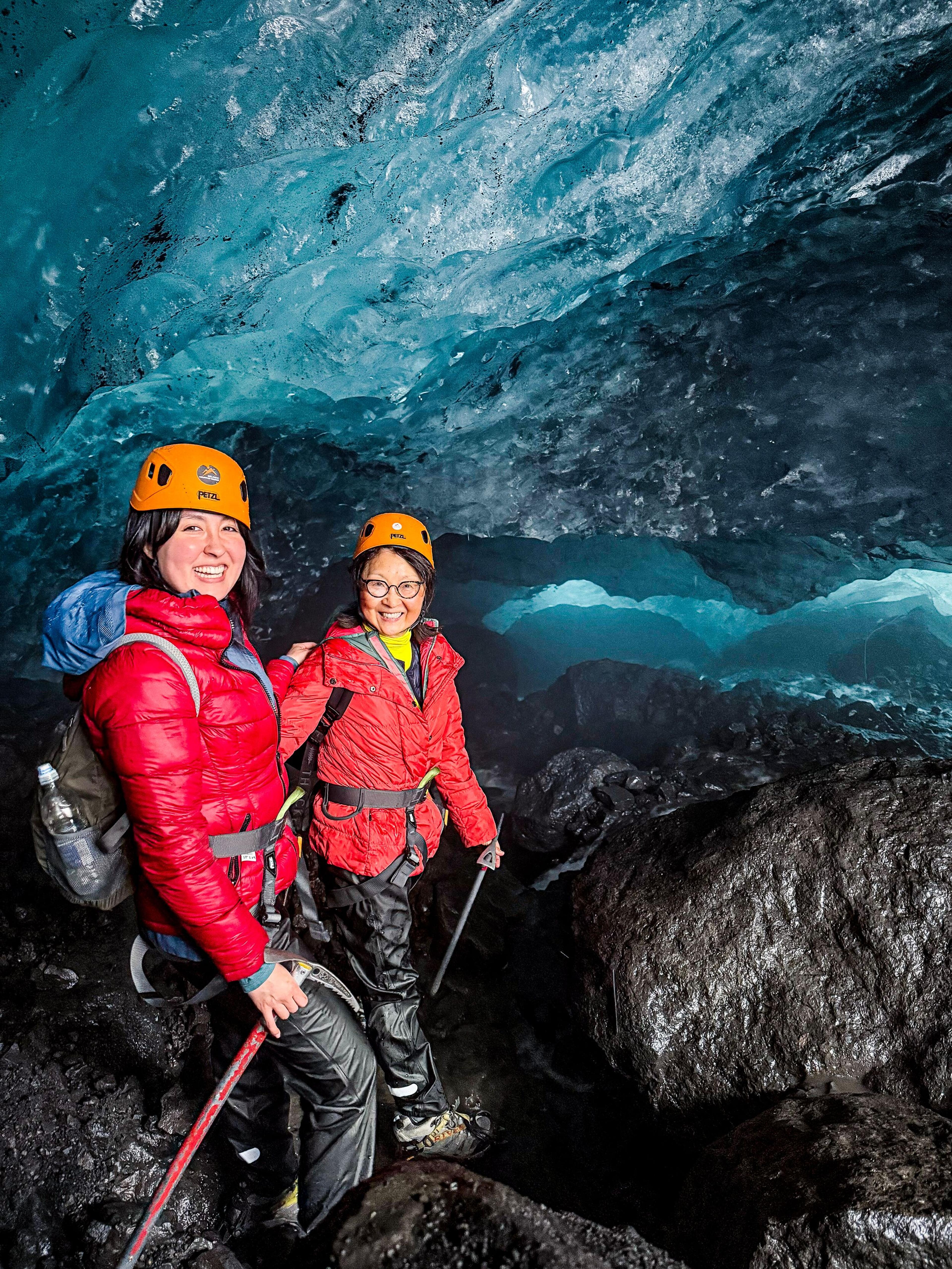 two women wearing helmets are standing in an ice cave