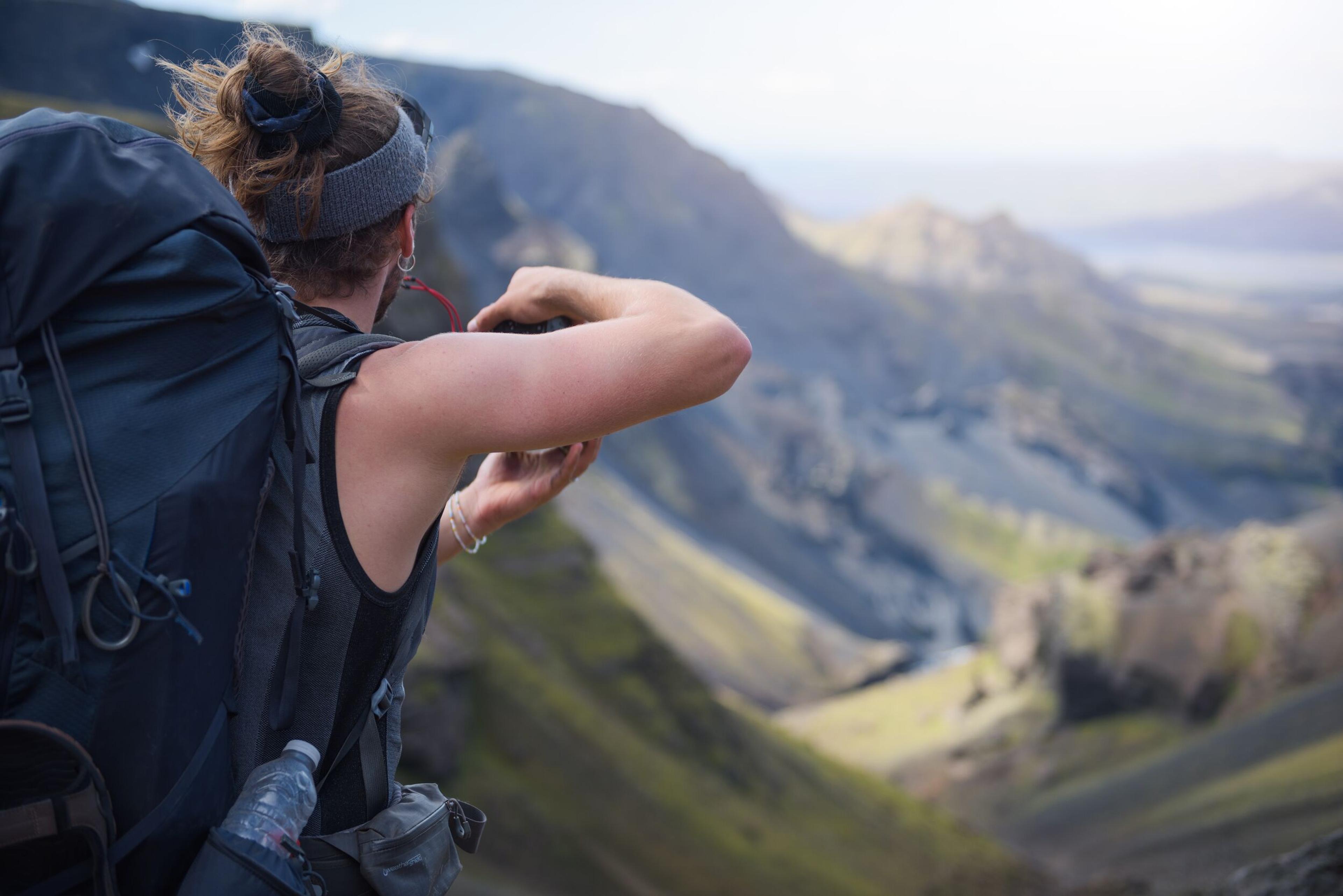 A hiker with a backpack looks out over a dramatic volcanic landscape, capturing the scene with a camera.