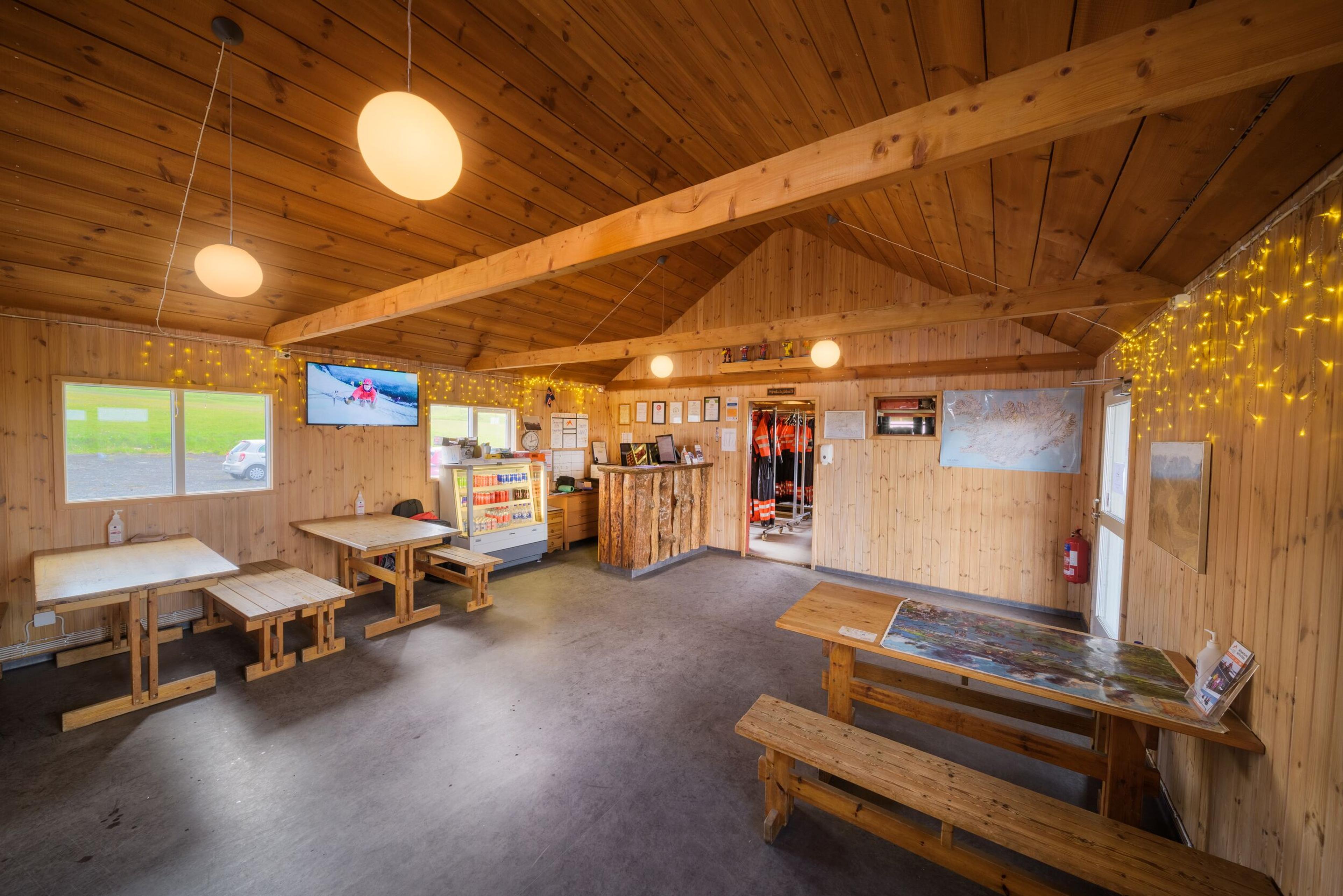 Rustic wood-paneled common room with wooden tables, a reception counter, and life jackets.