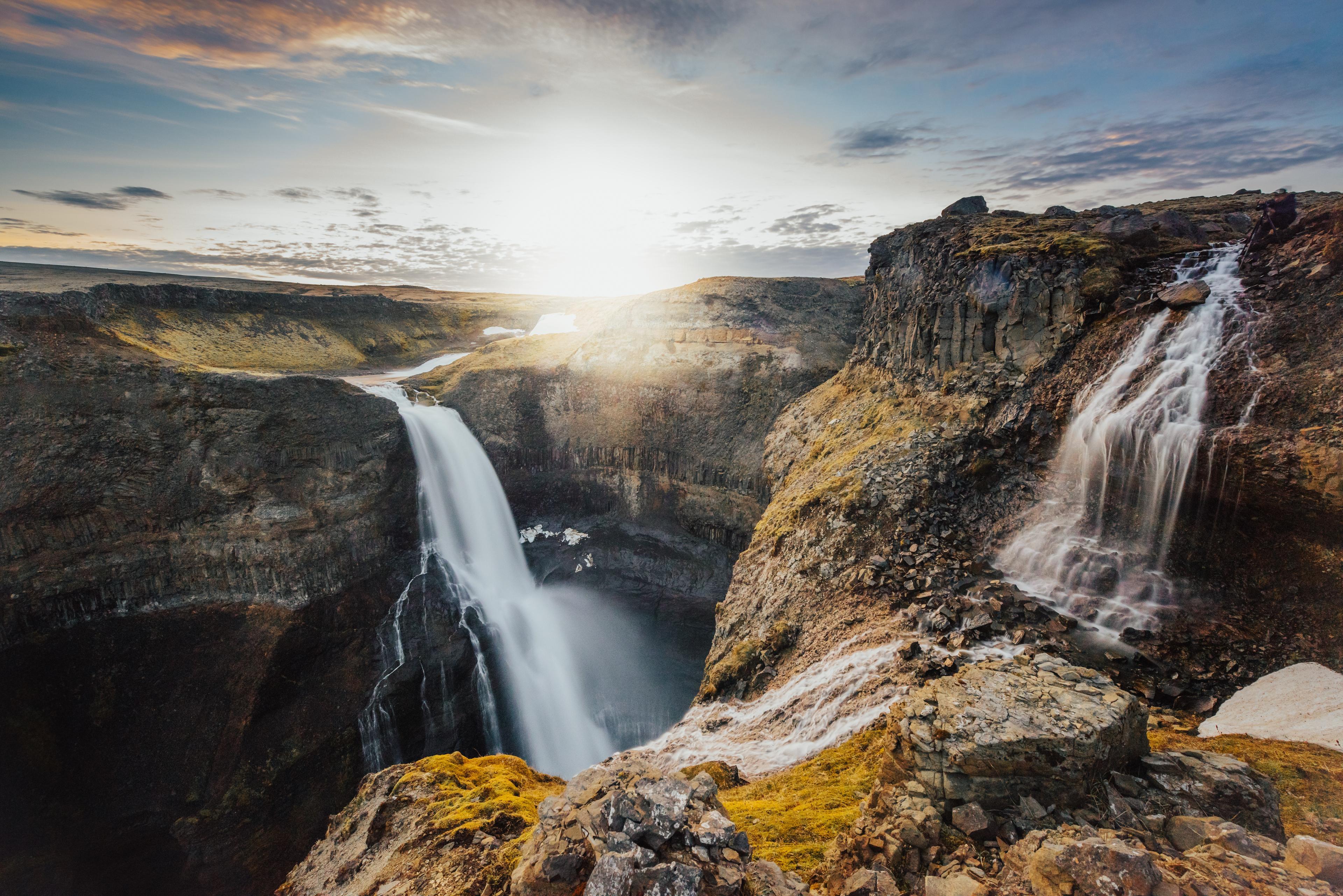 Two waterfalls cascading into a deep gorge between cliffs covered by brown moss