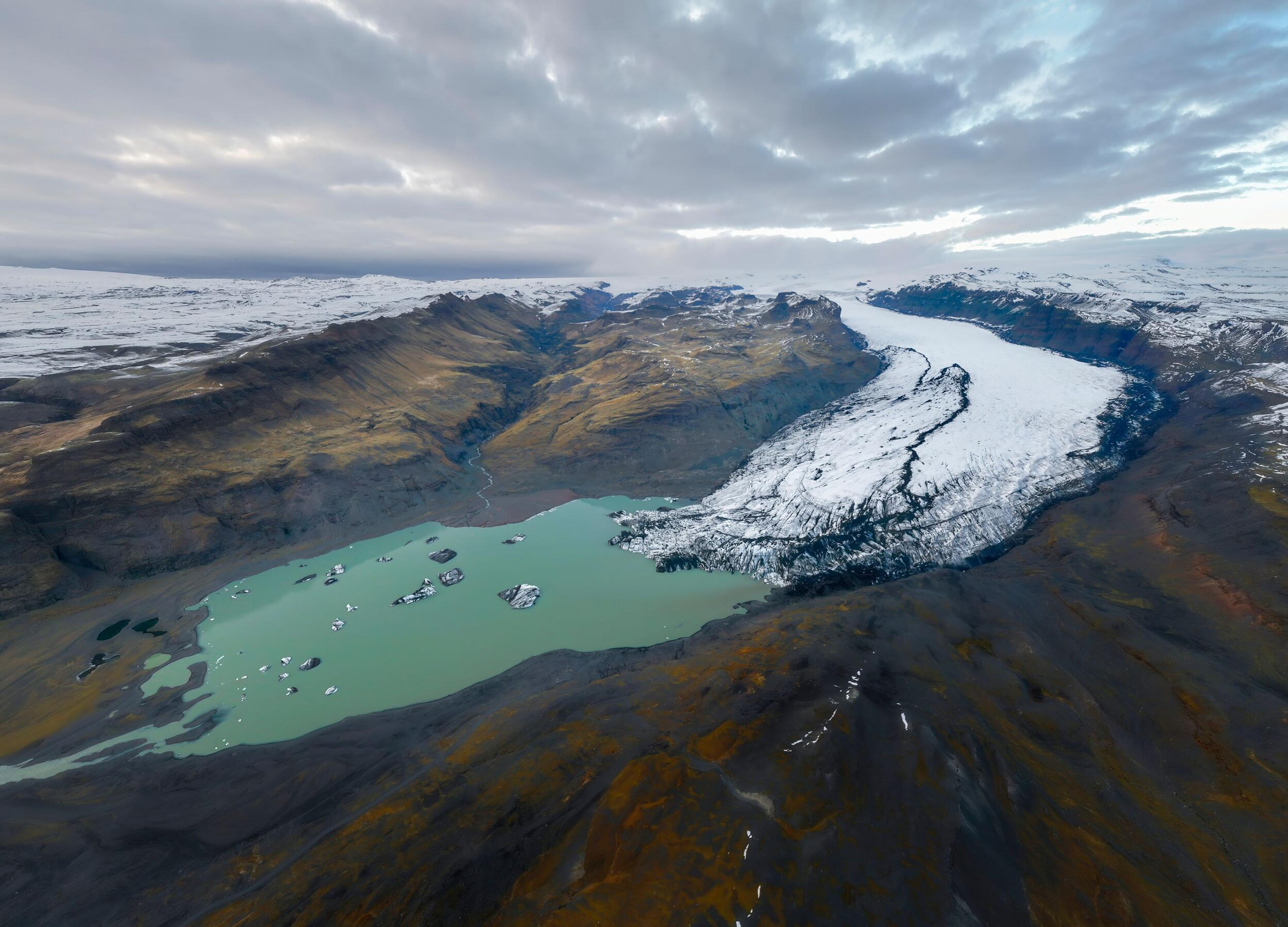 Aerial view of a glacial lagoon with floating icebergs, surrounded by mountains and a massive glacier, perfect for kayaking in Iceland.