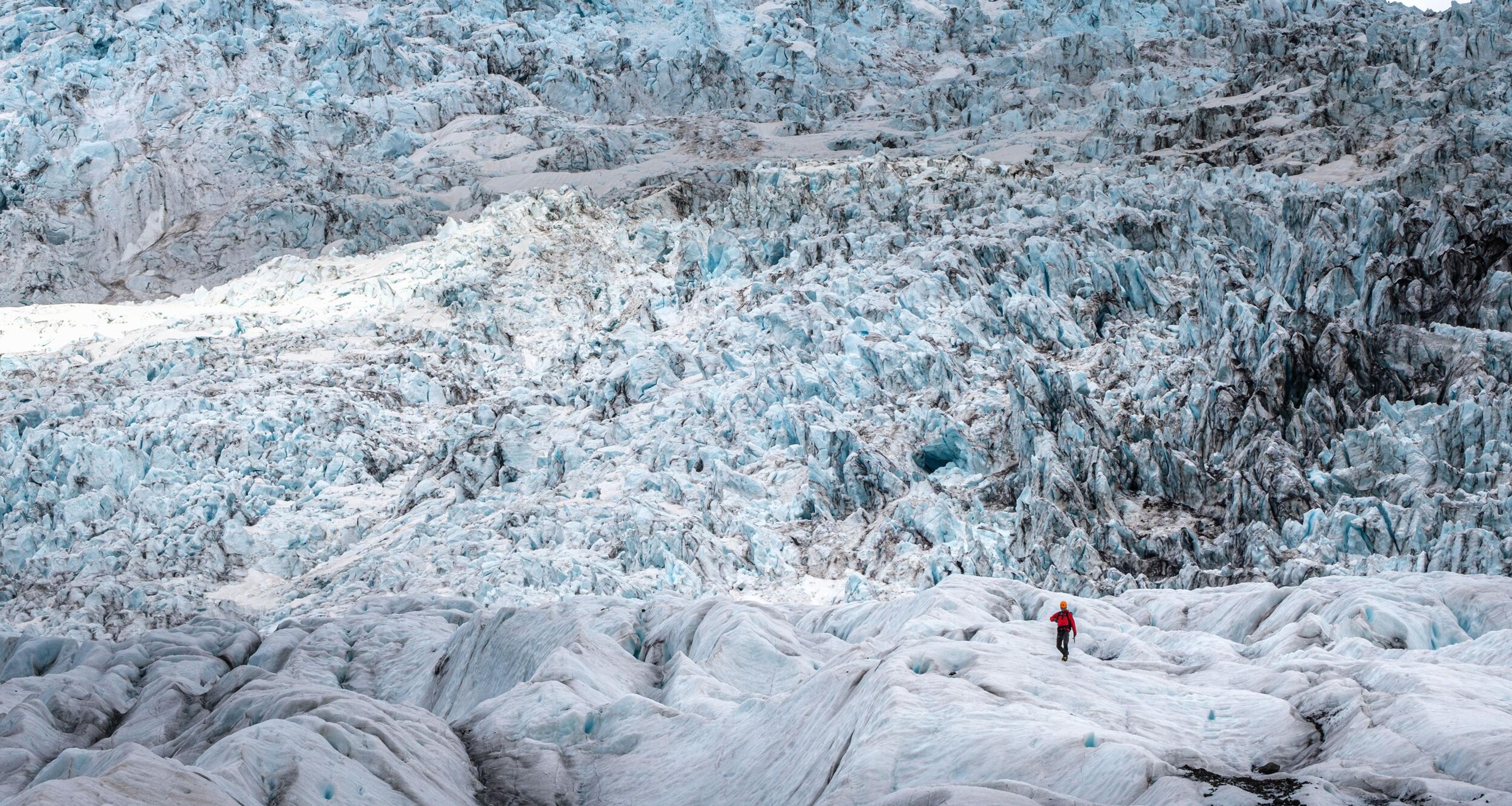 Tiny figure of a hiker amidst the vast and towering ice ridges of Falljökull glacier.