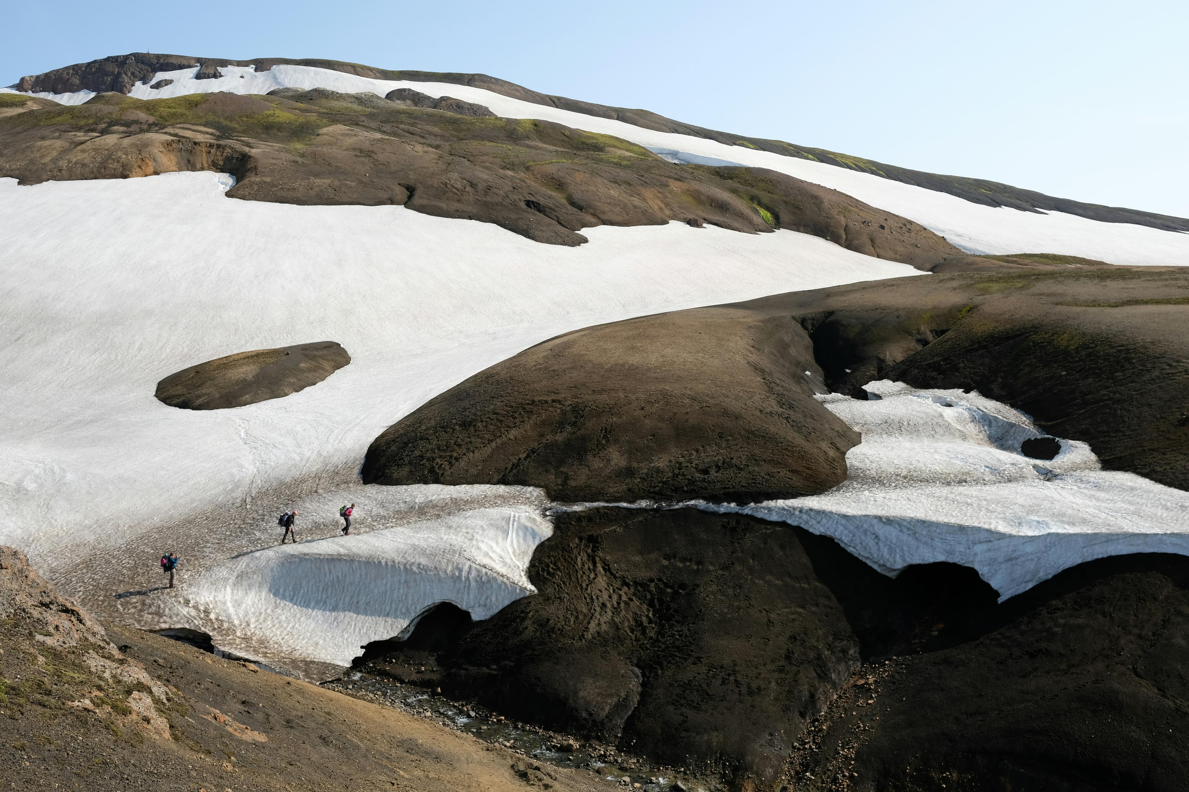 Hikers exploring snow-covered and volcanic rock terrain in the Icelandic Highlands, highlighting the contrasting landscape.