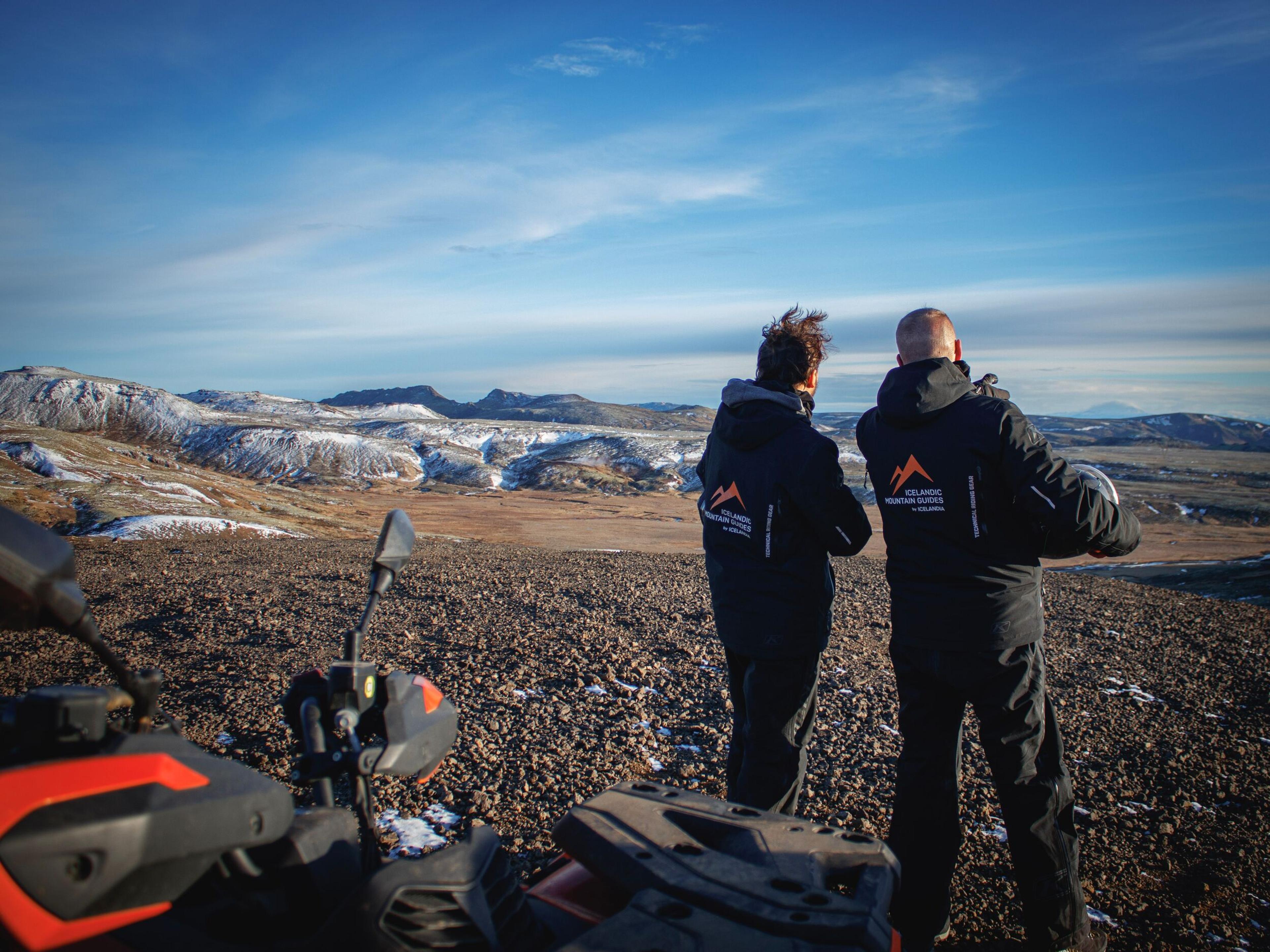 Person on an orange ATV in a snowy volcanic landscape at sunset.