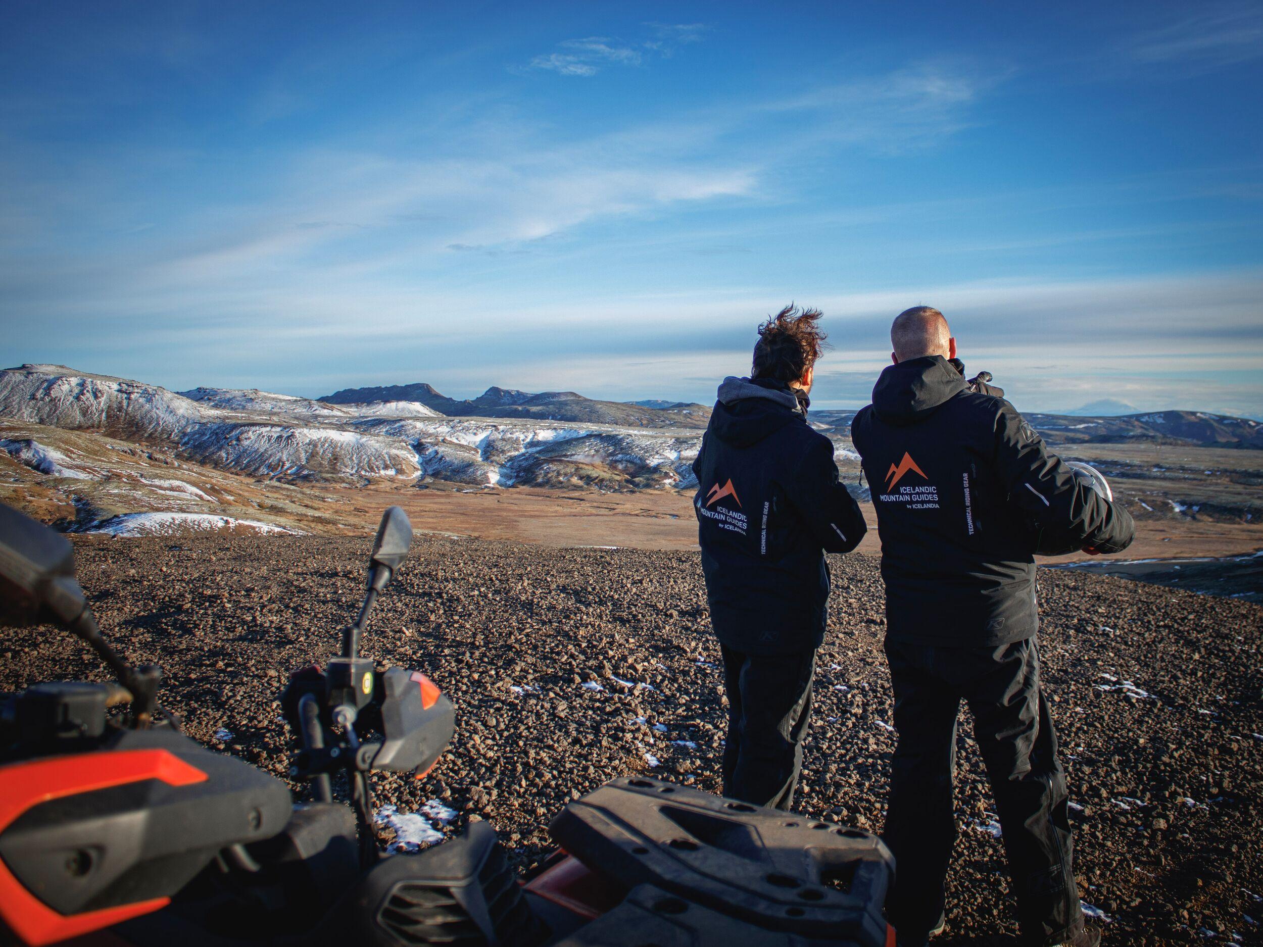 Person on an orange ATV in a snowy volcanic landscape at sunset.