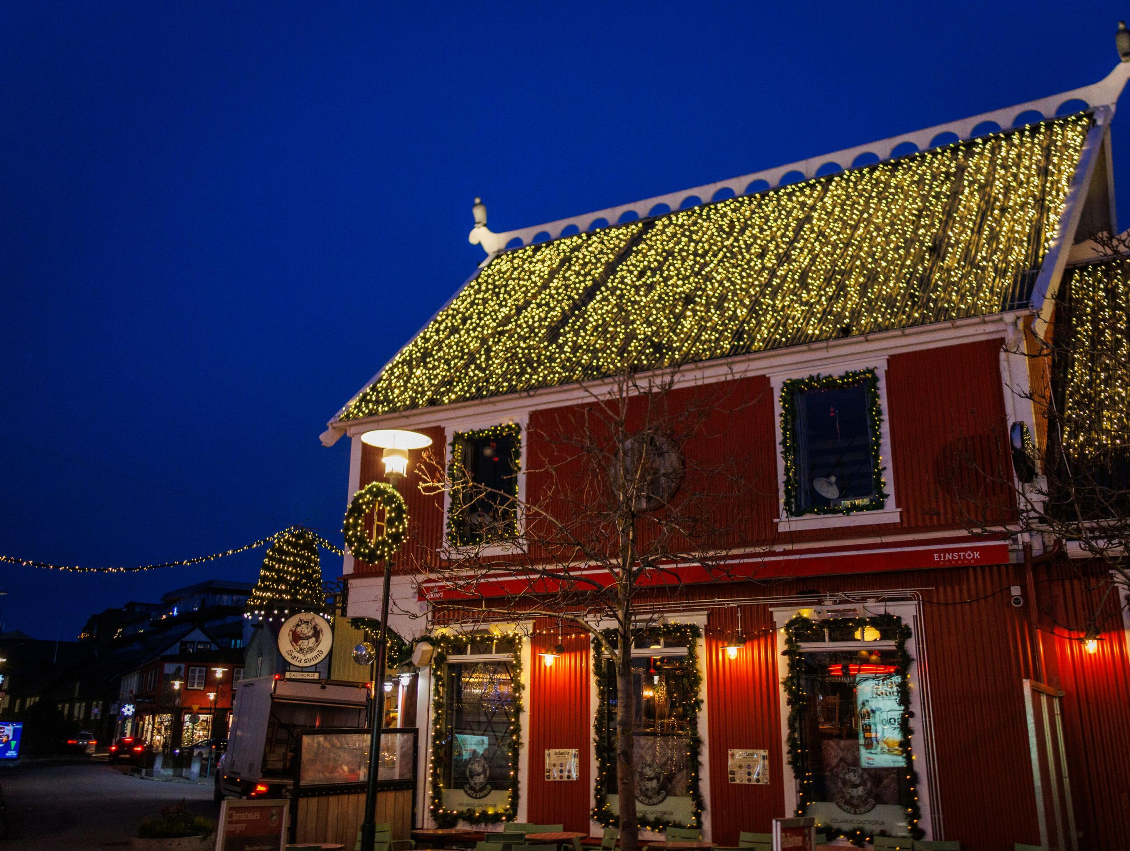 A red building brightly lit with golden string lights covering its roof and festive garlands at night.