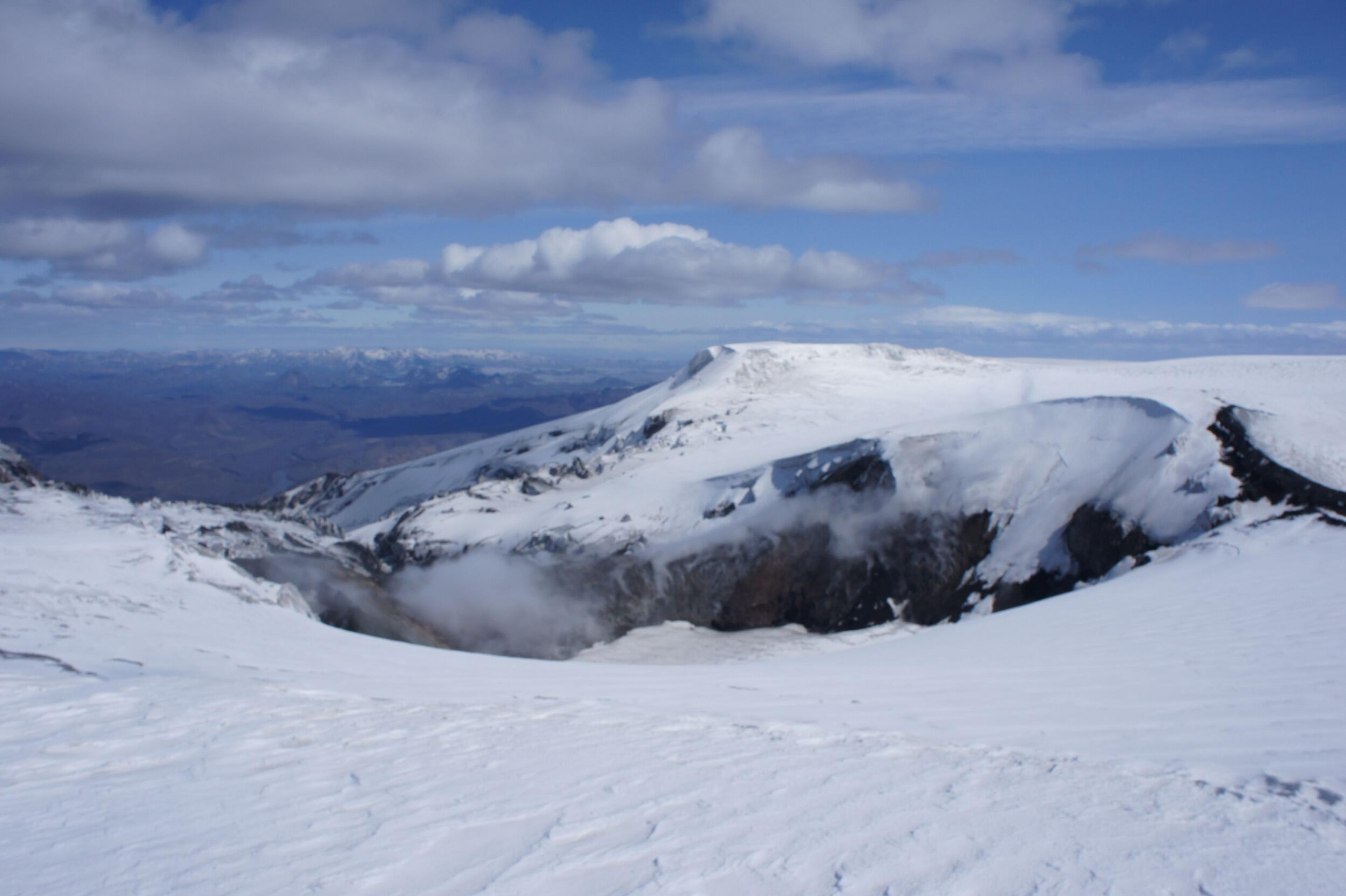 A sweeping view of the snow-covered Eyjafjallajökull glacier under a partly cloudy sky, with distant mountains visible on the horizon.