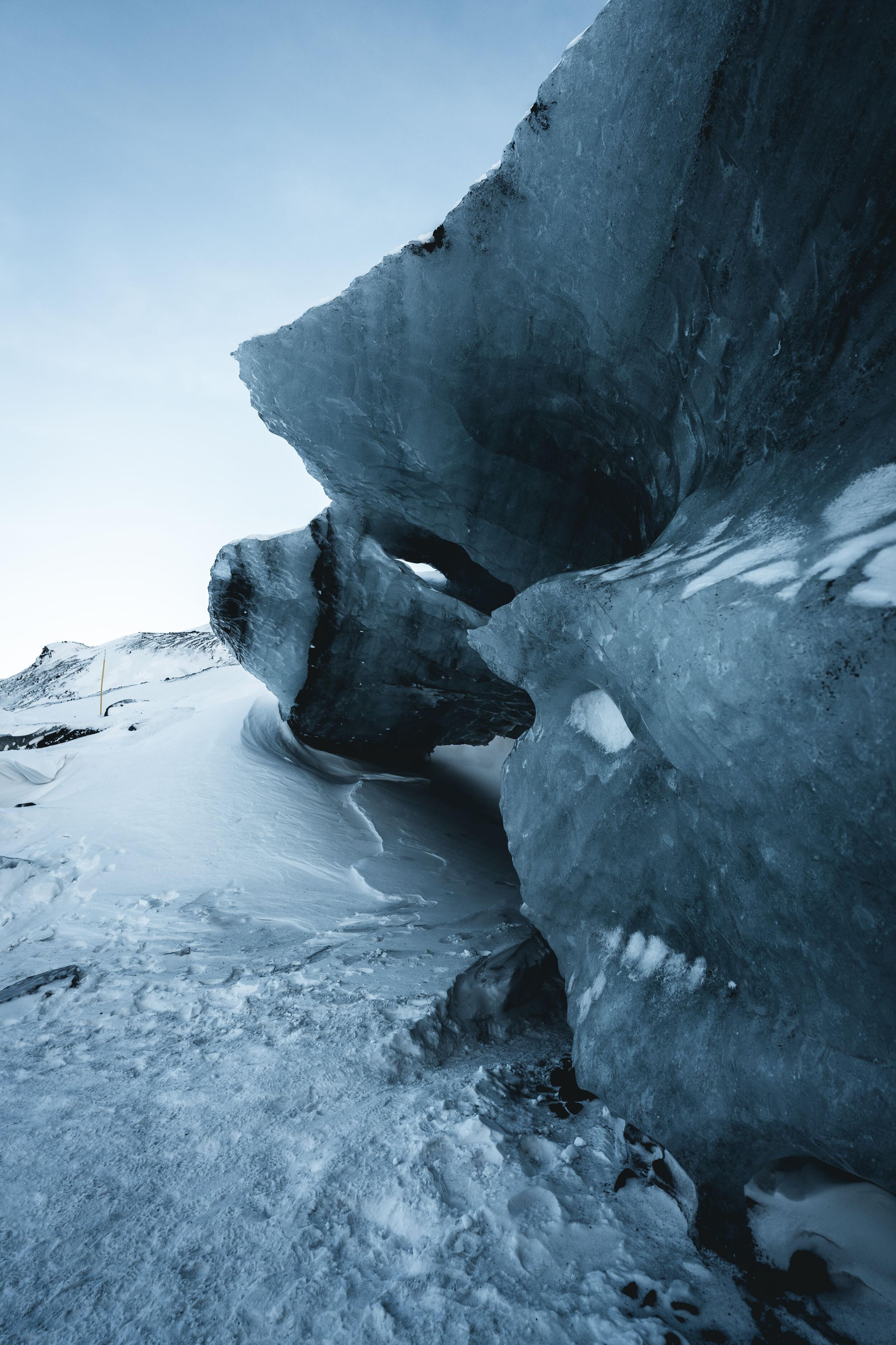 Massive ice formations at the edge of Mýrdalsjökull glacier, with snow-covered ground and a clear sky.