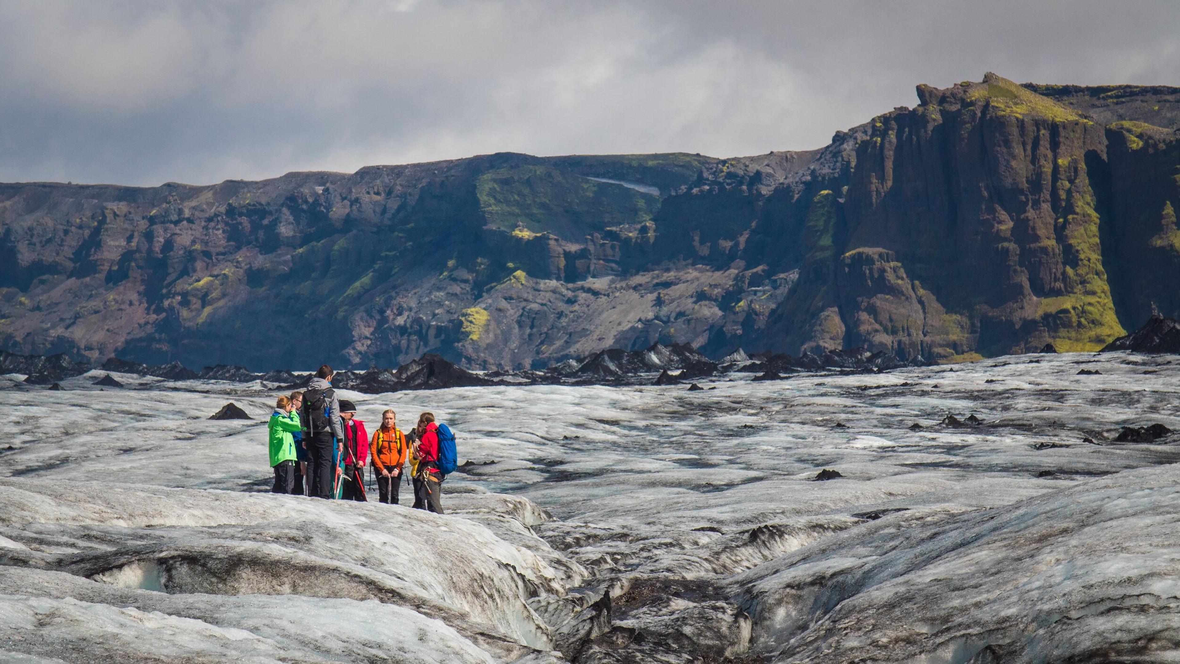 A group of hikers wearing helmets and carrying ice axes carefully explore the rugged terrain of Sólheimajökull glacier. A breathtaking Sólheimajökull glacier hike with views of deep crevasses and volcanic landscapes.