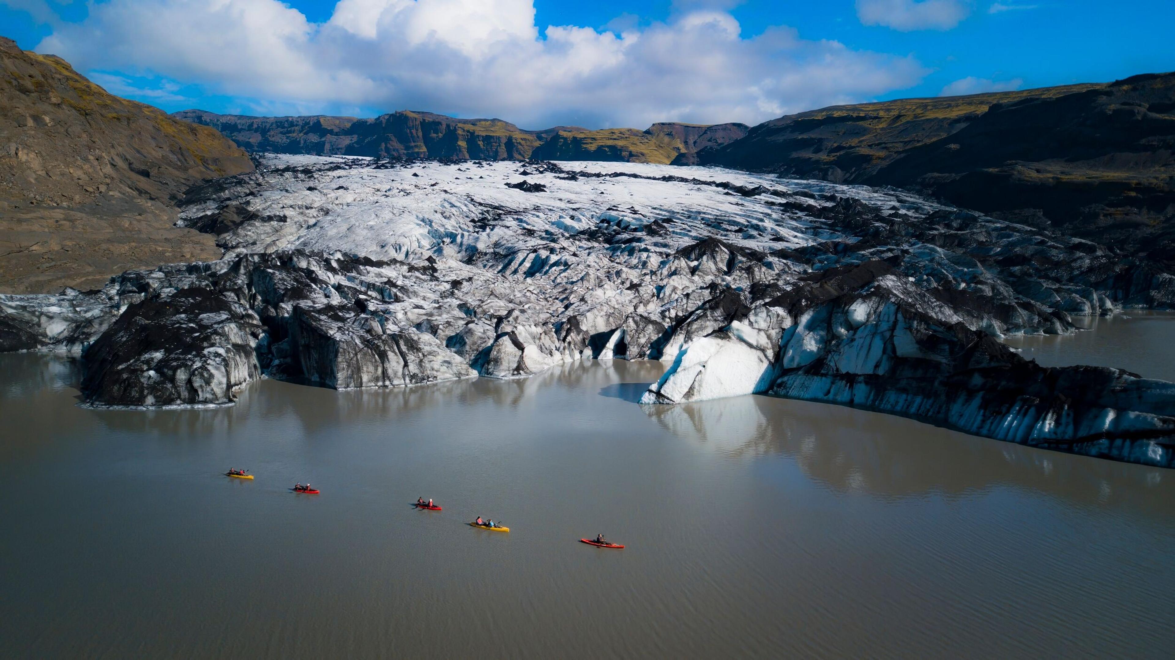 Five kayaks paddling across a serene lagoon, headed toward a breathtaking glacier in a stunning natural landscape