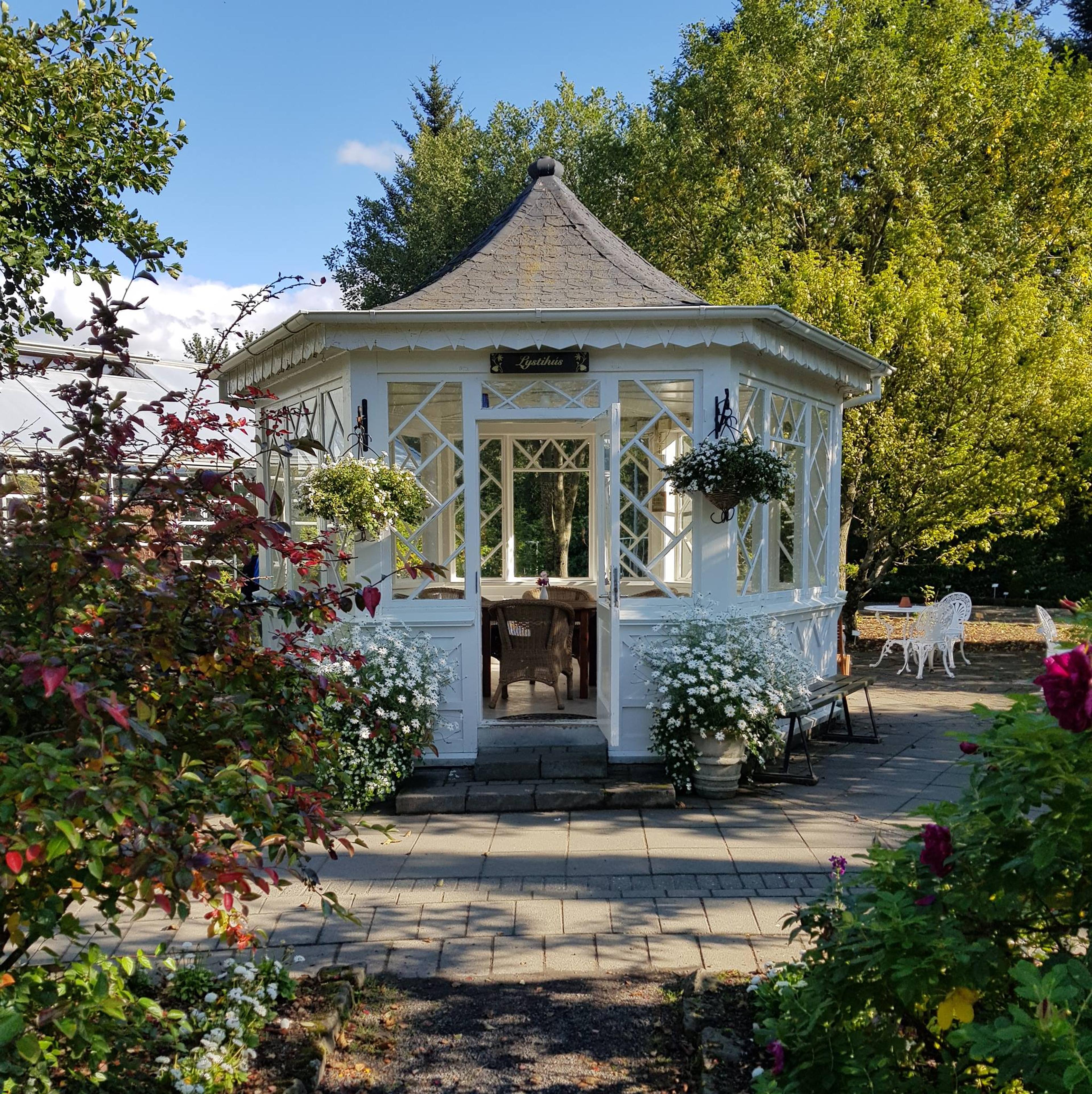 Charming white gazebo surrounded by blooming flowers and lush greenery on a sunny day.