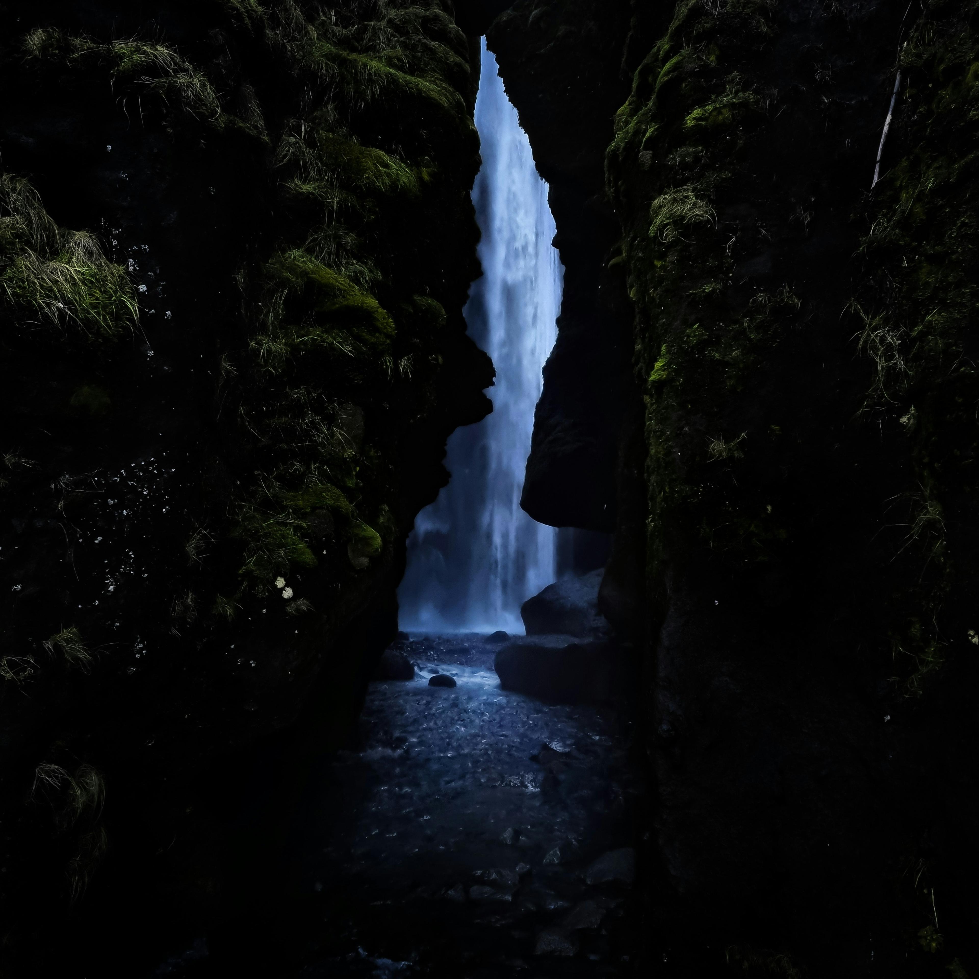 A hidden waterfall cascading down in a dark, moss-covered gorge creating a mystical and secluded atmosphere.