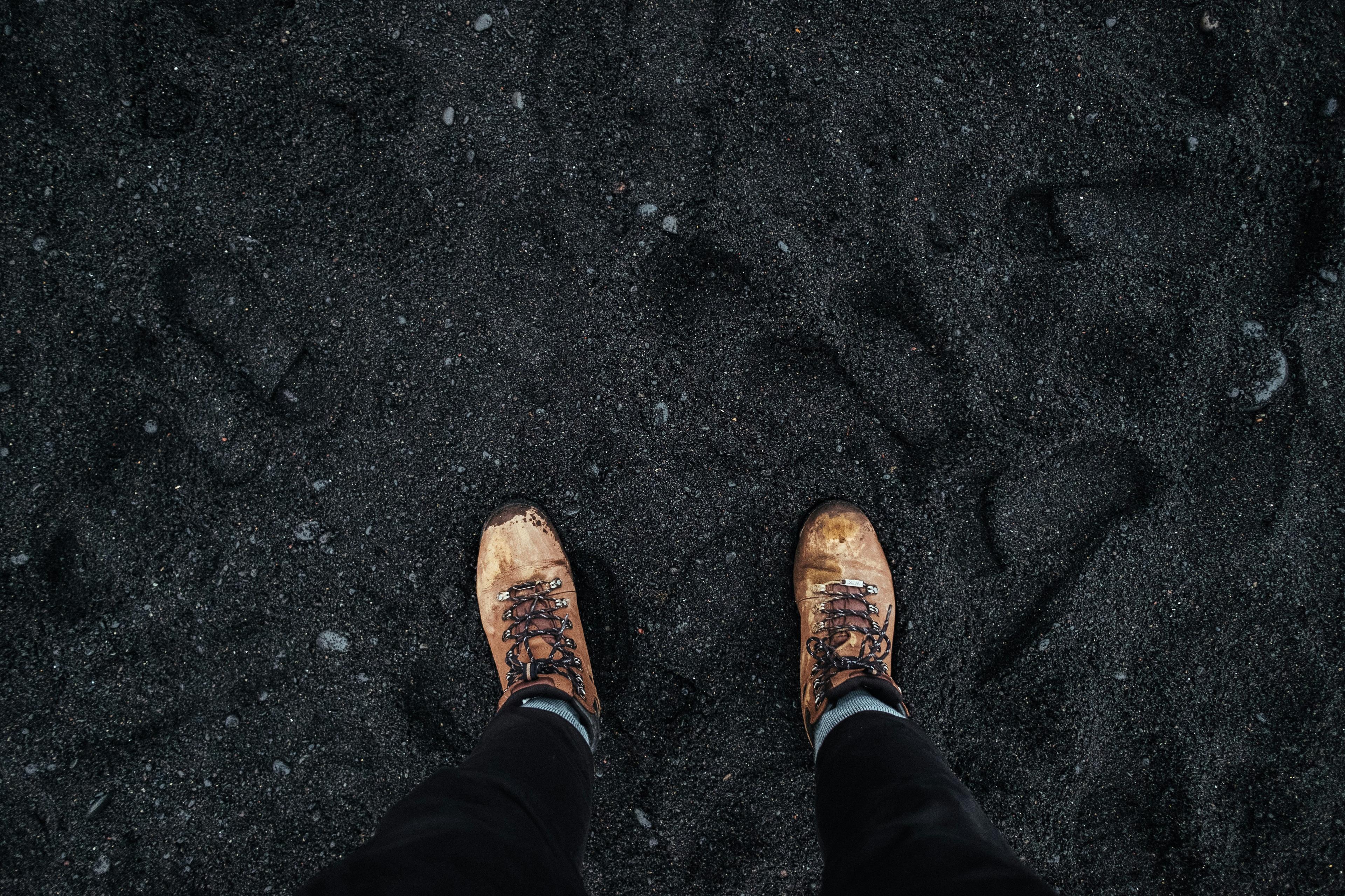  A close-up of hiking boots on the unique black sand of Reynisfjara beach, highlighting a stop on an Iceland South Coast tour.