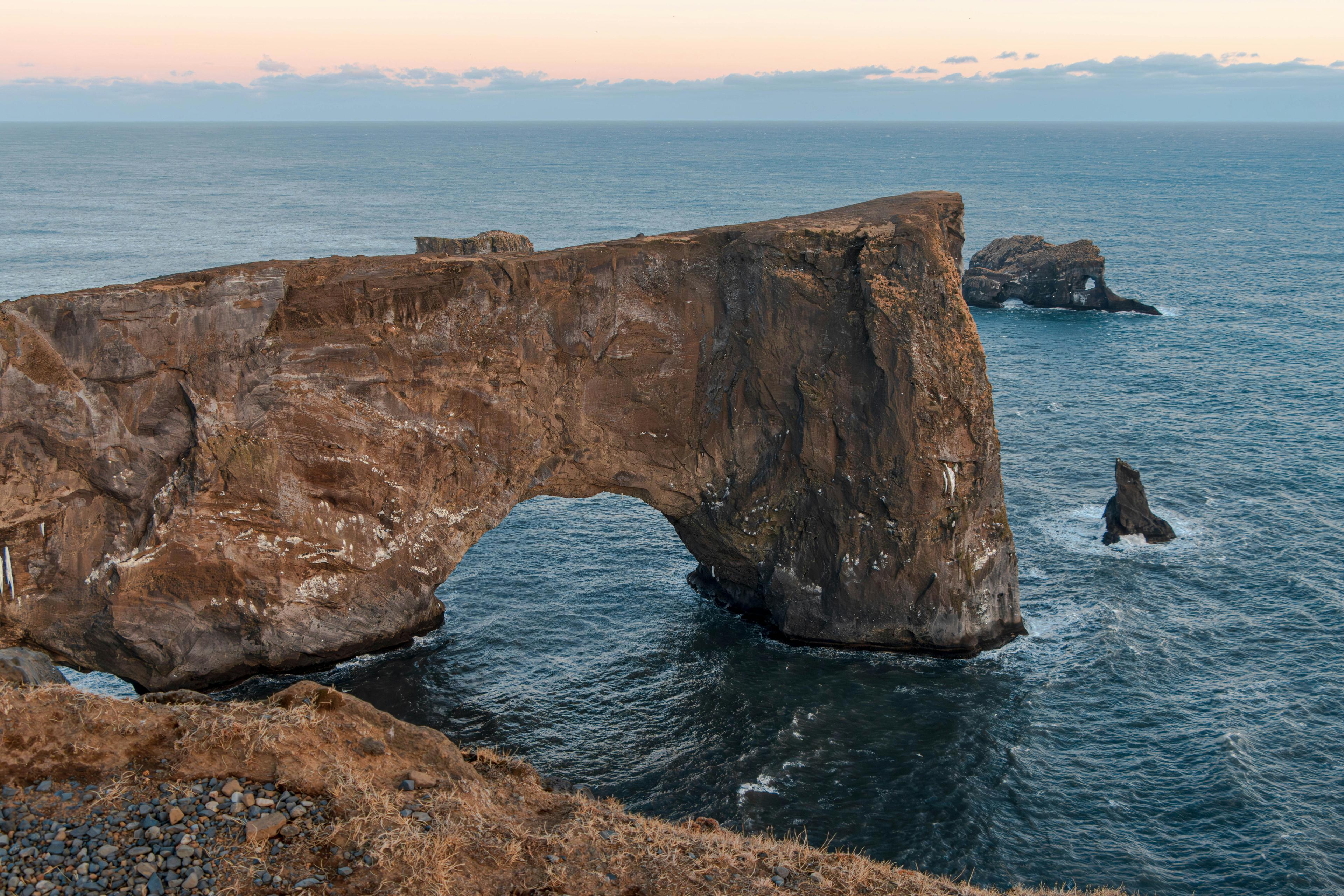 Rock arch formation at Dyrhólaey, Iceland, jutting into the ocean under a cloudy sky.