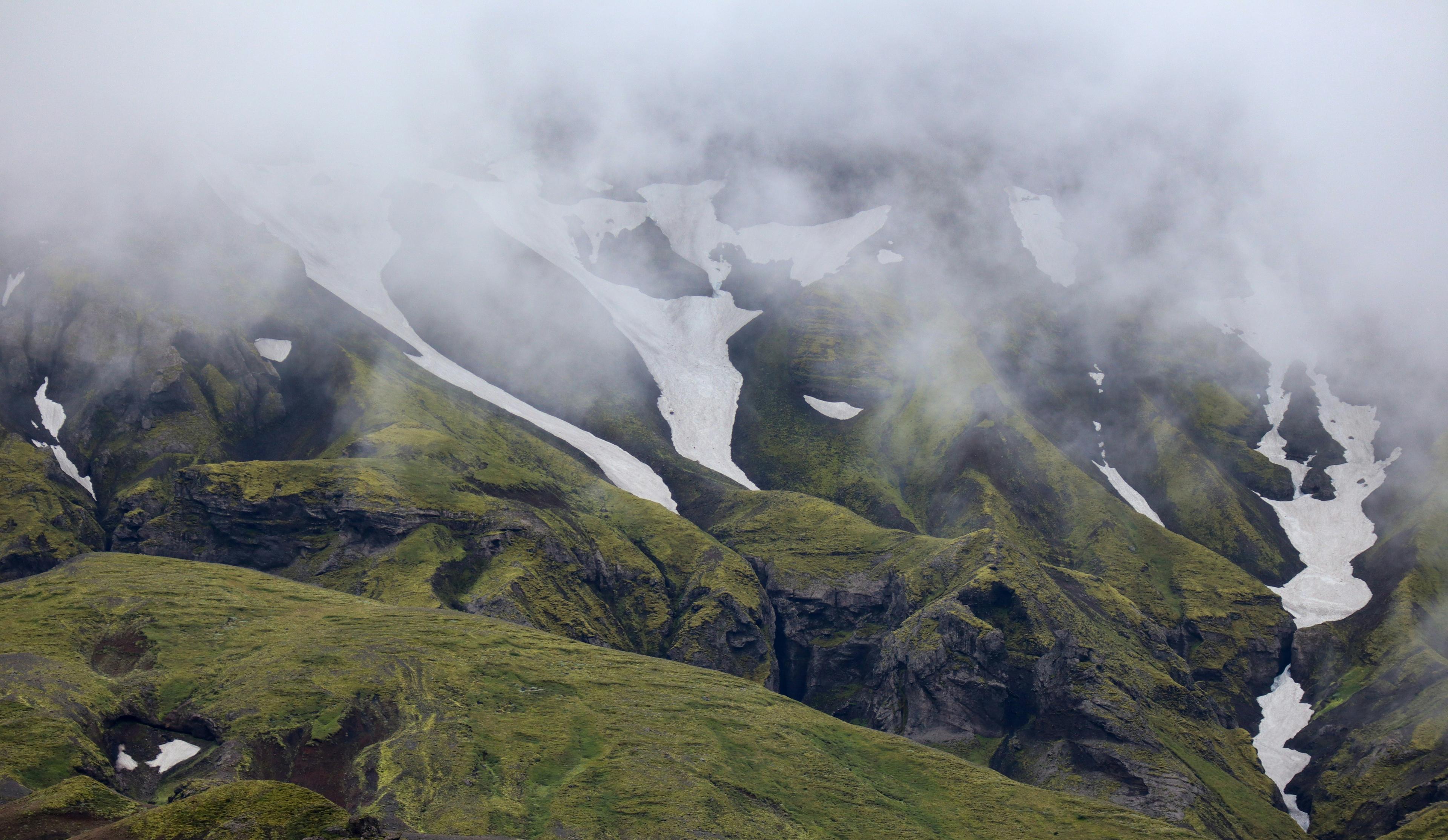 Fog-covered green mountains with patches of snow in Thorsmörk, Iceland.