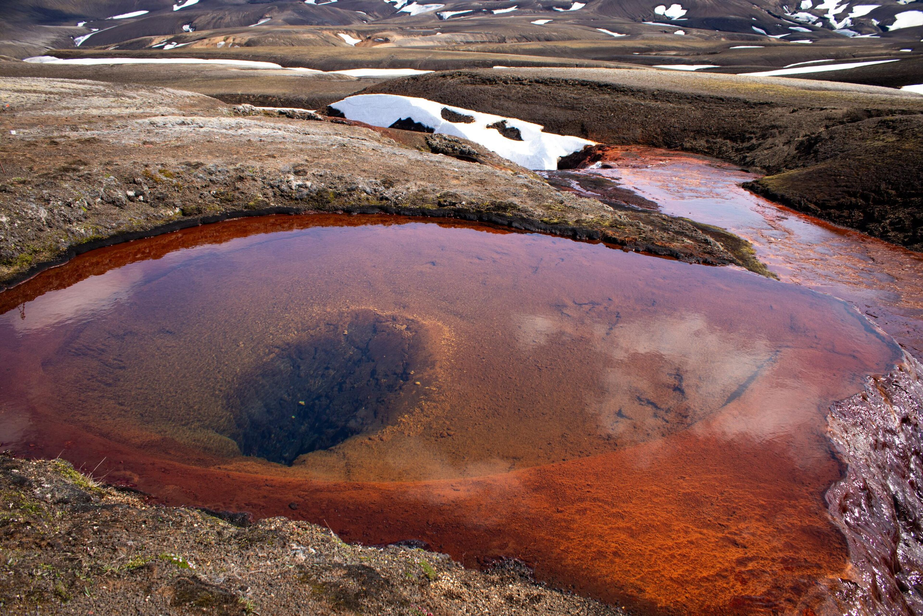 a large pool of red water in the middle of a desert .