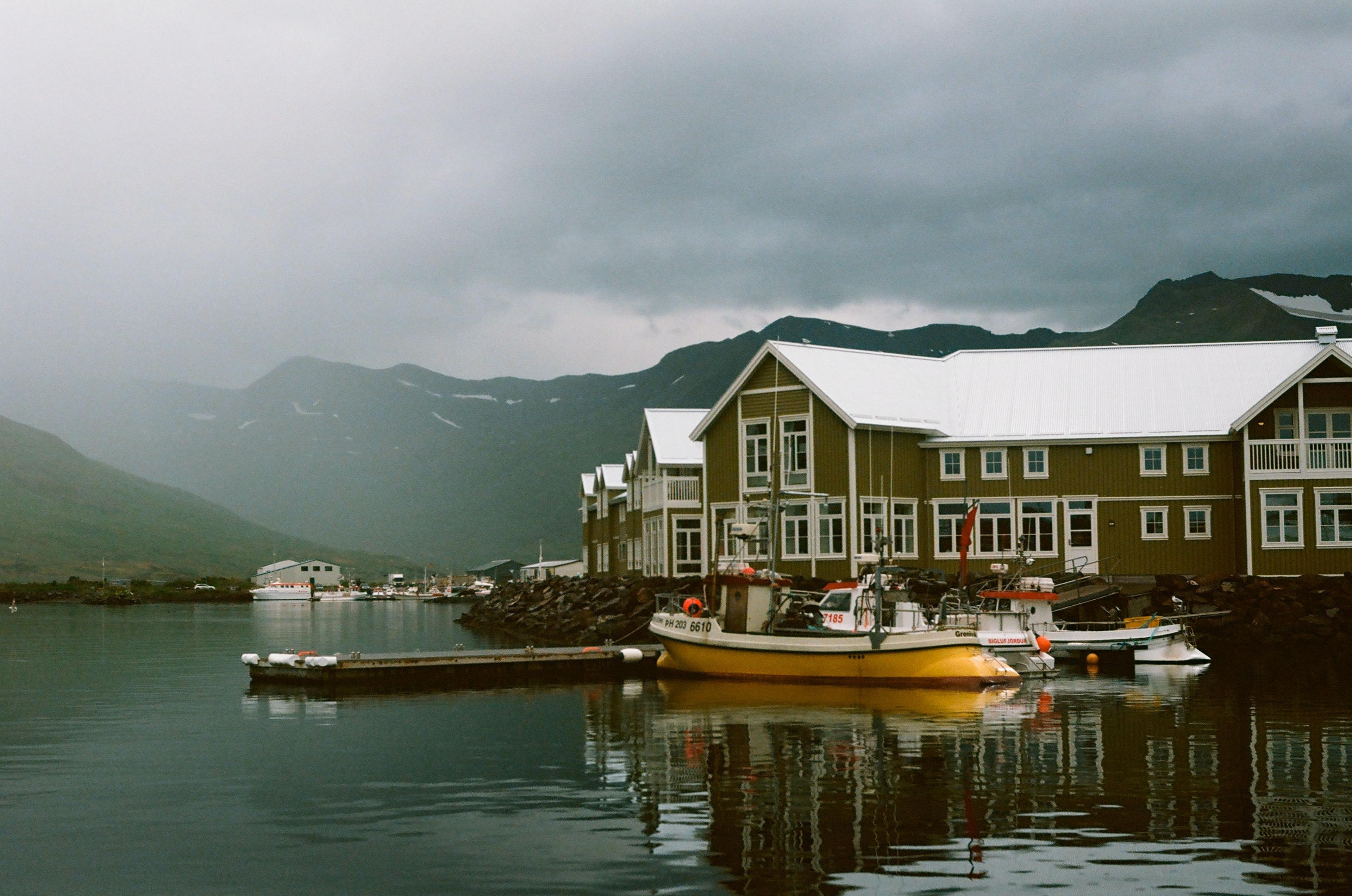 Traditional house situated on the edge of a tranquil sea bay, surrounded by small boats, with a misty and atmospheric landscape in the background