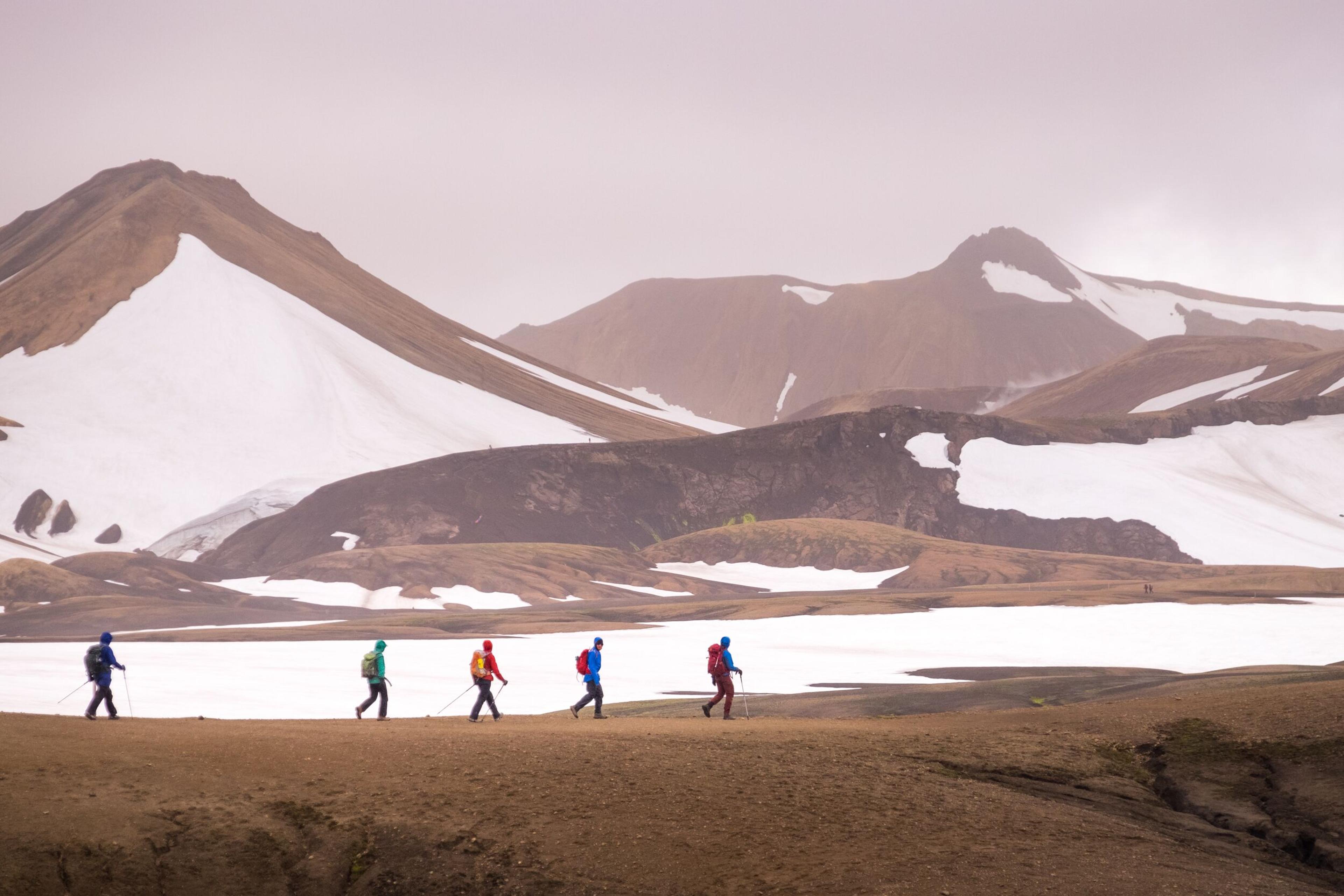 People trekking along the Laugavegur trail surrounded by brown and yellow hills dotted with snow patches