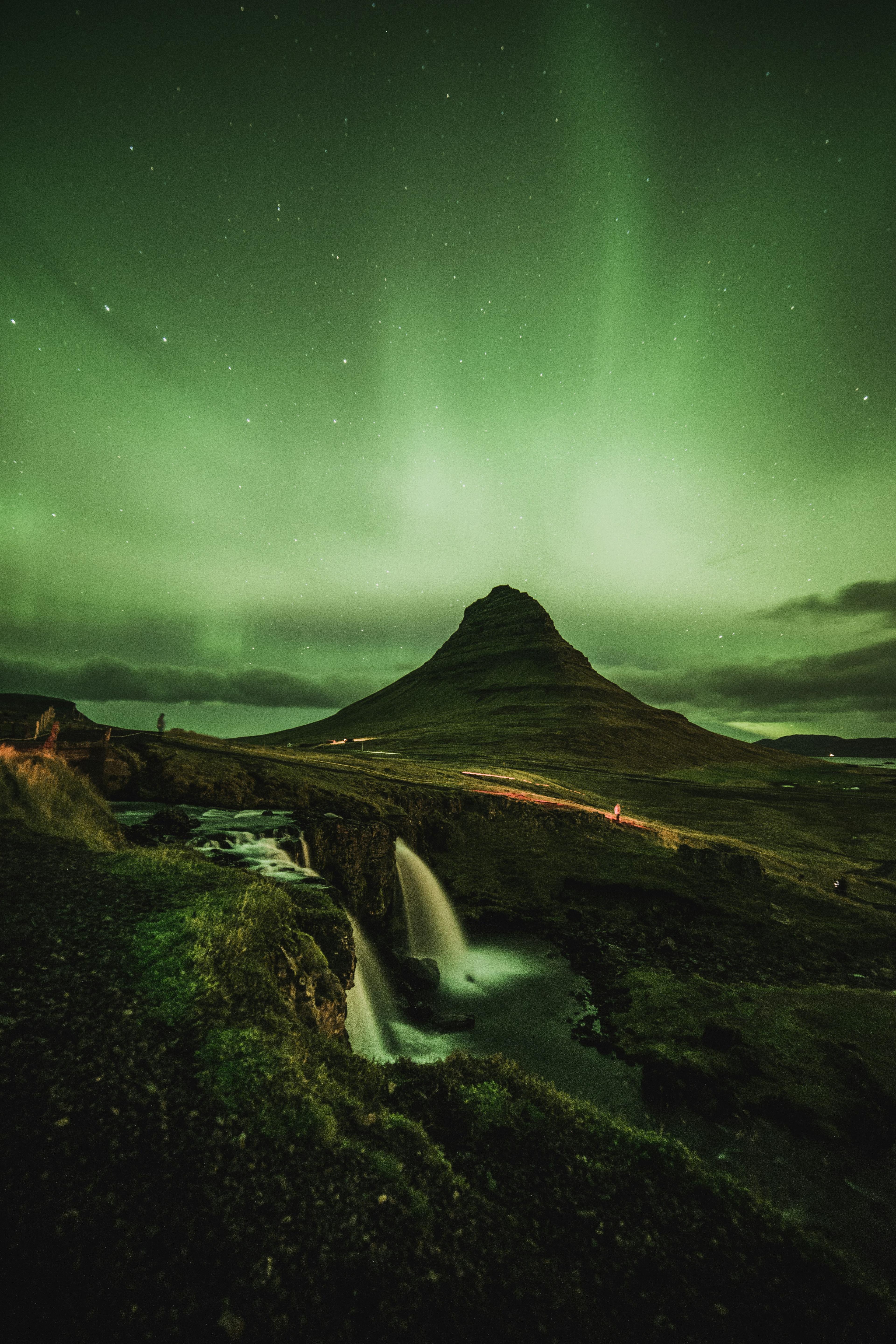 A stunning display of the Northern Lights over a waterfall with a mountainous landscape in the background.