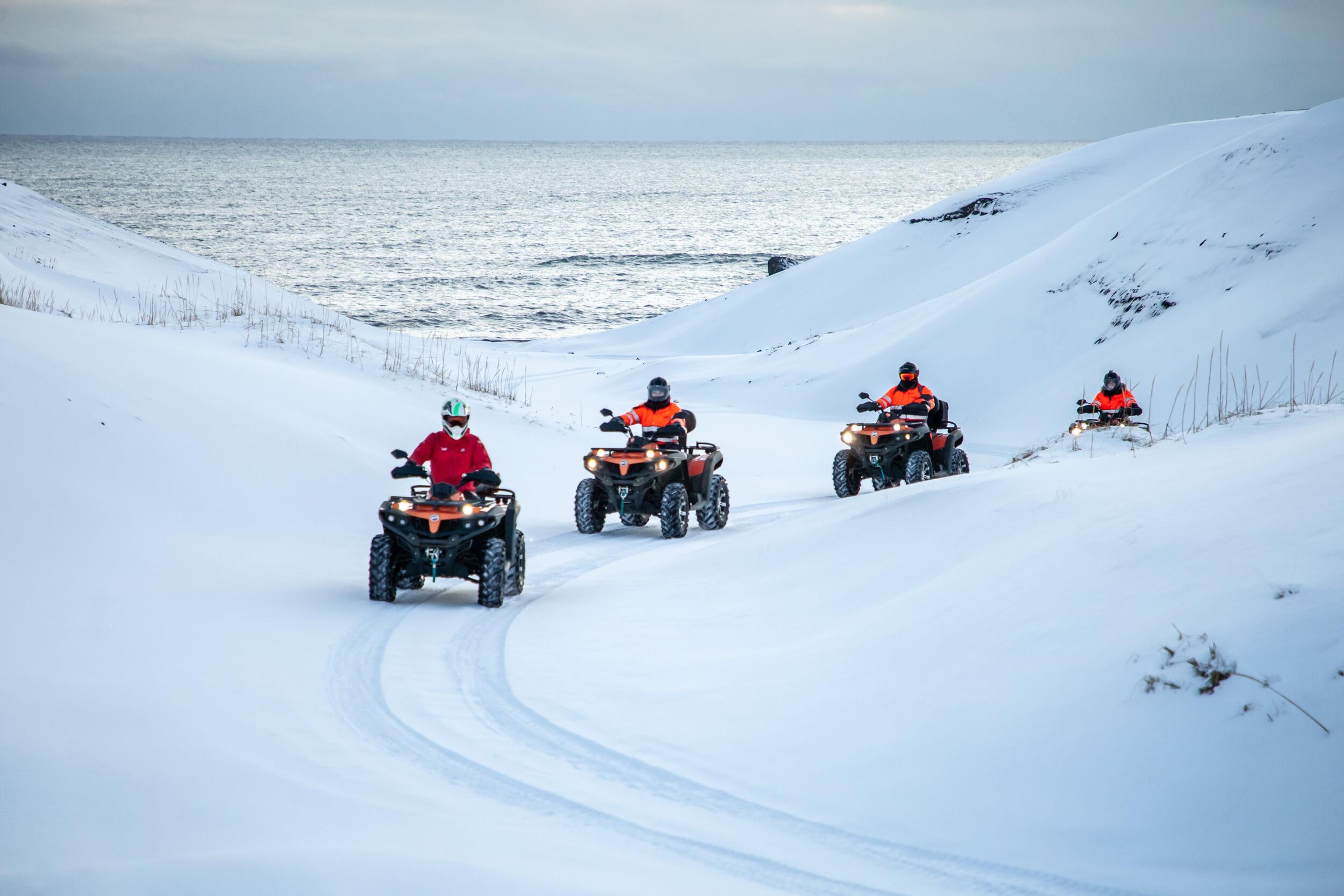 Four people driving atvs on the snow-covered black beach in the south coast of Iceland.