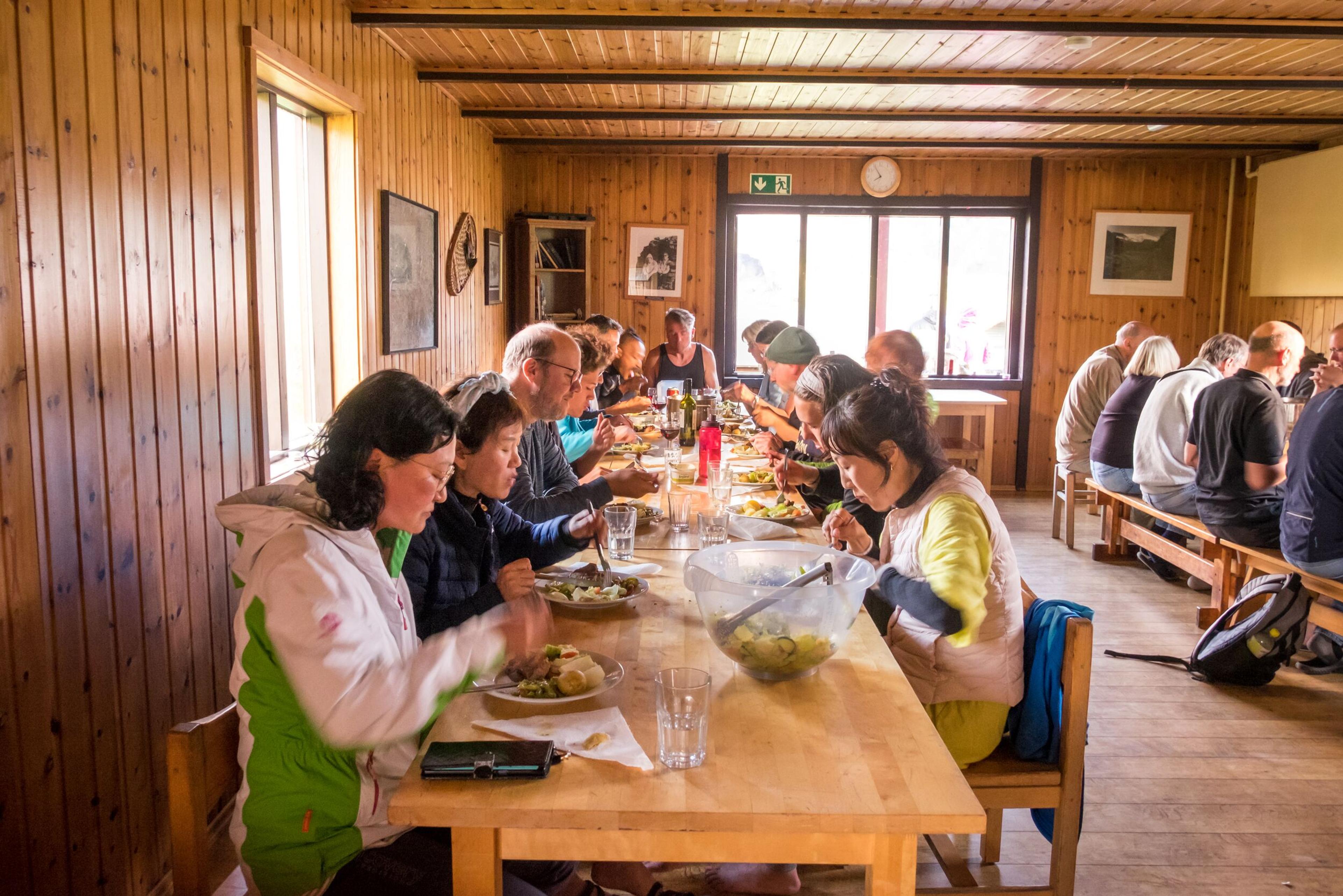 Group of people enjoying a meal inside a cozy wooden lodge in Landmannalaugar, Iceland.