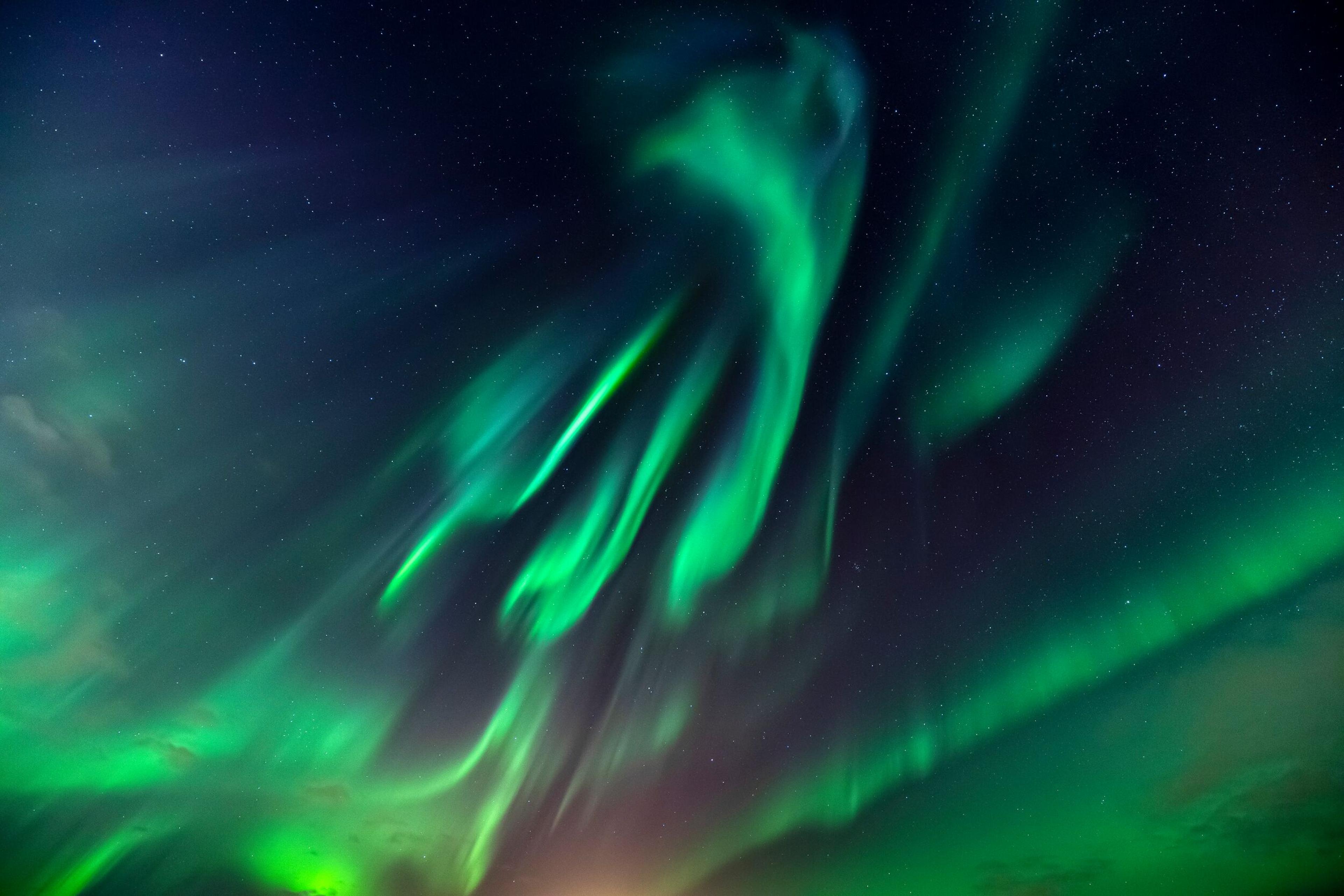 Ethereal green auroras sweeping across the night sky, with dynamic shapes and swirls, evoking the fluid motion of a celestial dance.