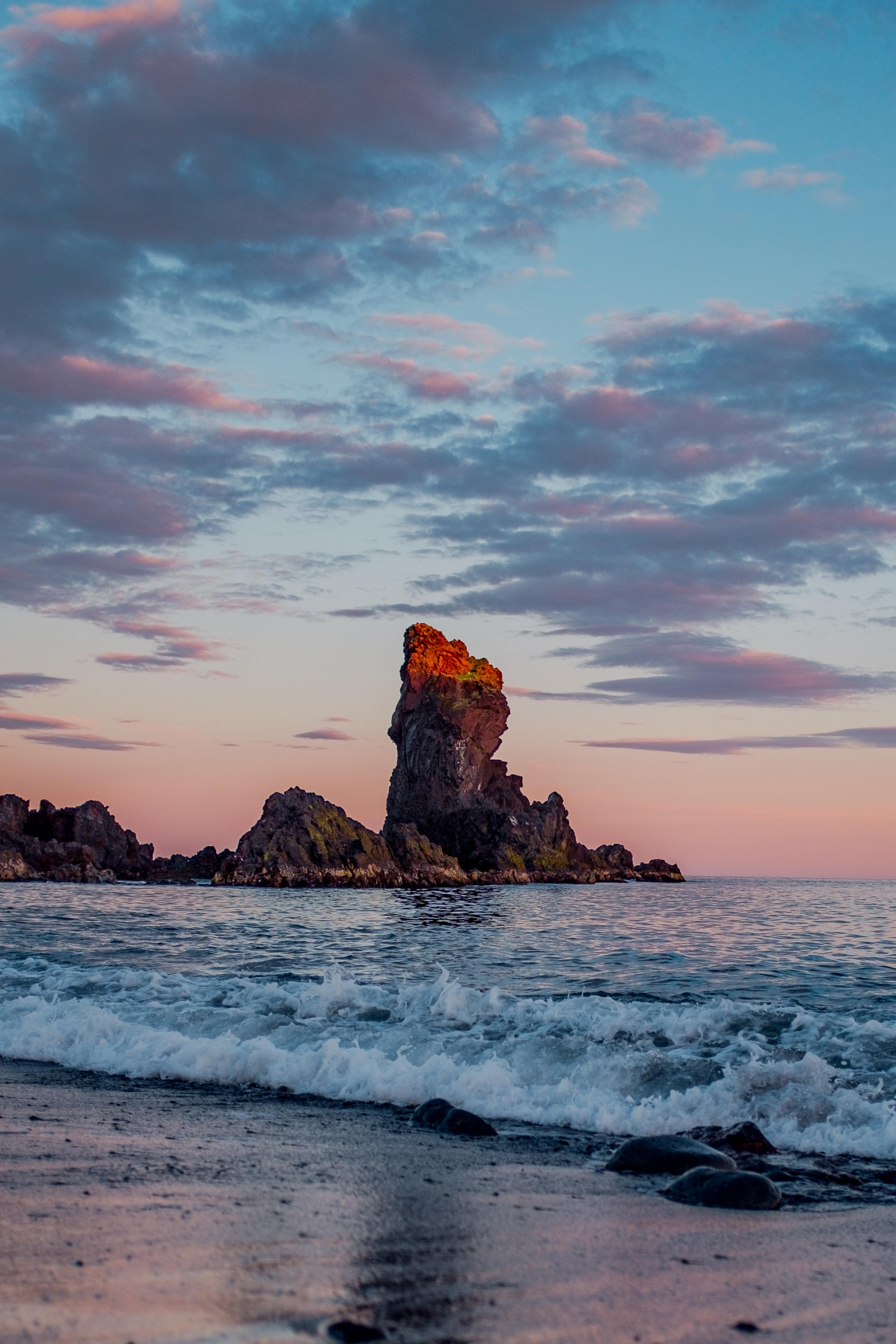 Imposing sea stack stands tall against a backdrop of the sky awash with warm sunset hues of oranges, pinks, and purples