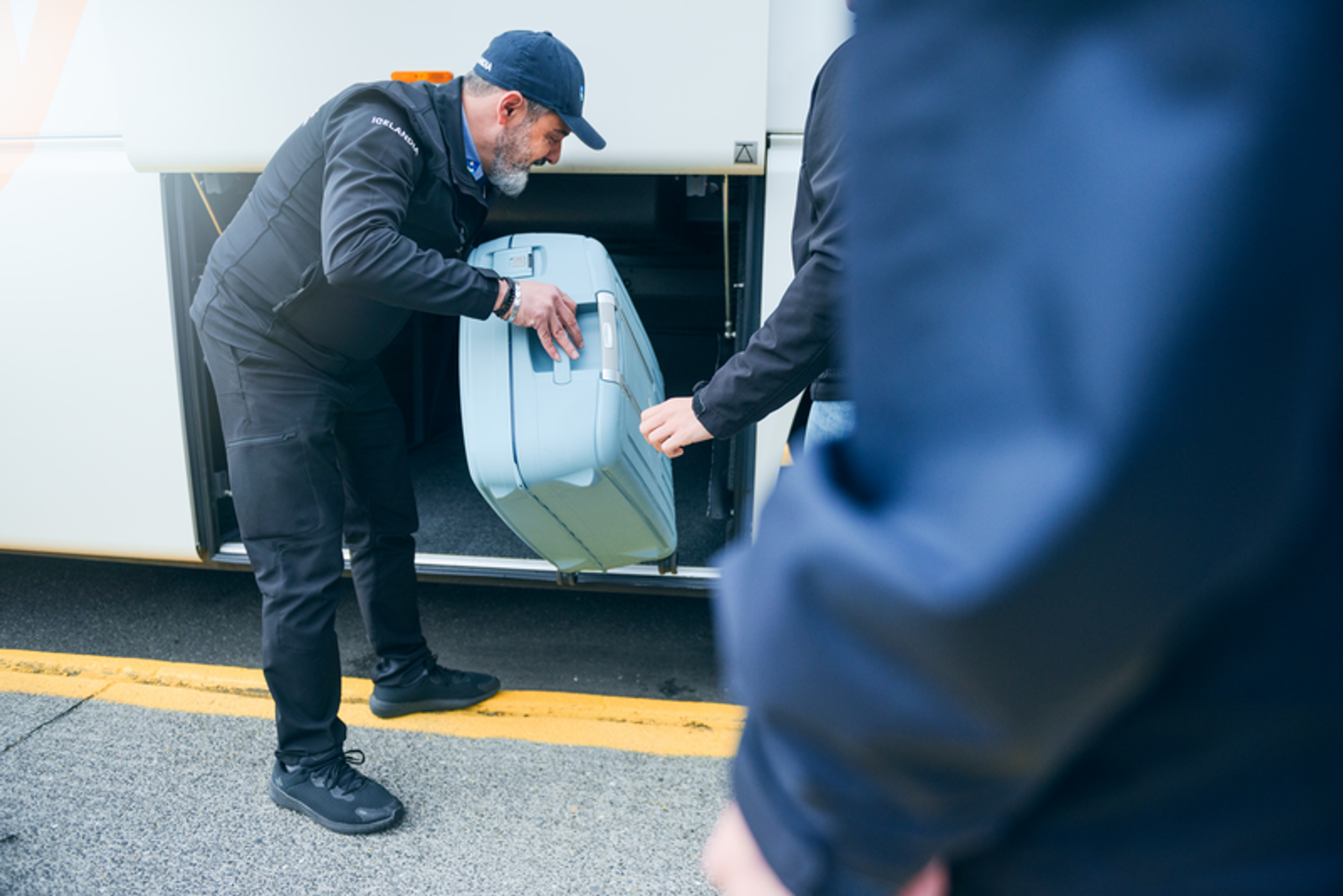 A bus driver is helping a passenger load a large suitcase into the luggage compartment of a bus.
