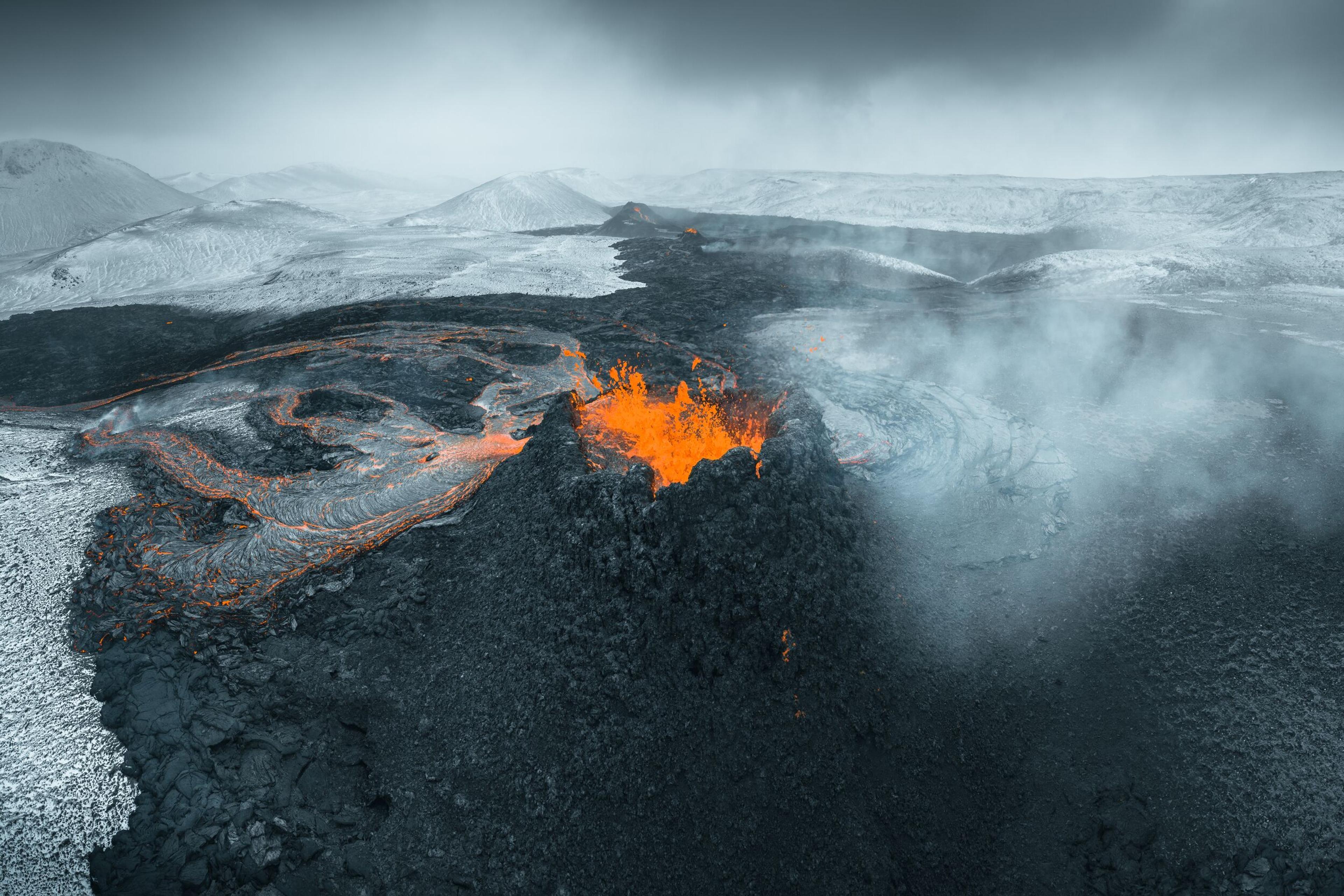 Contrasting view of a vibrant orange volcanic crater amidst a snowy landscape under a cloudy sky.
